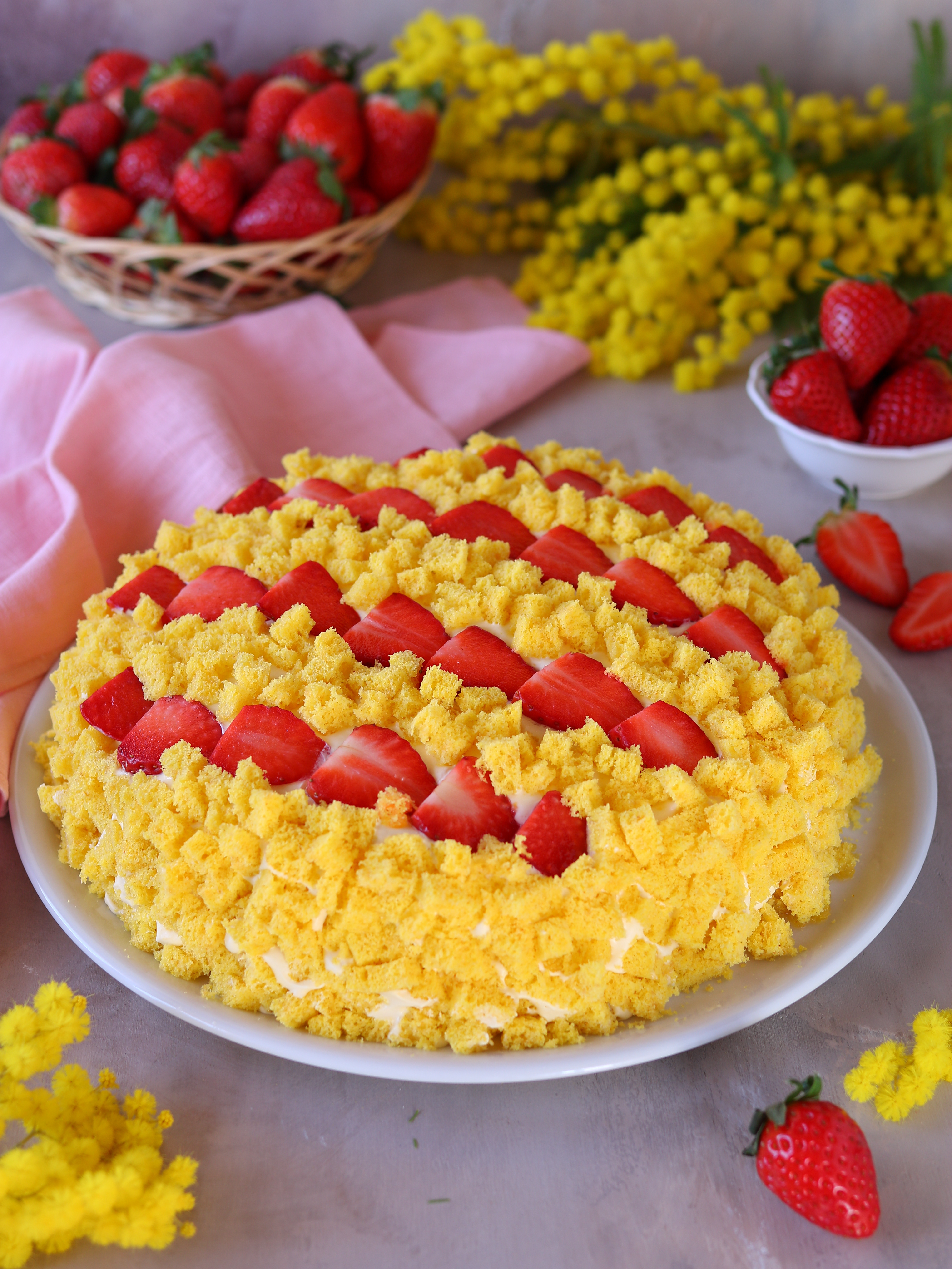 TORTA MIMOSA ALLE FRAGOLE Una ricetta facile e veloce, ideale da portare in tavola l’8 marzo, per la Festa delle Donne. Questa deliziosa e bellissima torta si realizza con pochi e semplici ingredienti: un pan di Spagna alto e soffice, una buonissima crema pasticcera arricchita da panna montata e tantissime fragole sono infatti gli elementi che compongono questo dolce. INGREDIENTI PER IL PAN DI SPAGNA 200 g farina 00 200 g zucchero 5 uova 8 g lievito per dolci PER LA CREMA DI FARCITURA 4 cucchiai farina 00 4 cucchiai zucchero 2 uova 1 cucchiaino curcuma facoltativo 1 scorzetta di limone 500 ml latte 200 ml panna montata zuccherata PER LA BAGNA E LA DECORAZIONE 400 g fragole 1 limoni il succo 2 cucchiai zucchero 100 ml acqua PROCEDIMENTO Iniziamo preparando le fragole per il ripieno e la bagna della torta. Tagliamo a pezzetti le fragole (teniamone qualcuna da parte per la decorazione) e mettiamole in una ciotola. Condiamole con il succo di limone e due cucchiai di zucchero. Lasciamo insaporire le fragole per almeno mezz’ora. Intanto prepariamo il pan di Spagna: in una ciotola capiente rompiamo le uova, aggiungiamo lo zucchero e lavoriamo con lo sbattitore elettrico fino a ottenere un composto spumoso. Aggiungiamo la curcuma alle uova. La curcuma serve solo per dare un colore giallo intenso al pan di Spagna, quindi se volete potete anche non metterla. Sempre lavorando con lo sbattitore elettrico, aggiungiamo la farina poco per volta. Infine aggiungiamo anche il lievito. Ottenuto un impasto liscio e omogeneo, trasferiamolo in una teglia rotonda unta e infarinata del diametro di 24 centimetri. Cuociamo il pan di Spagna in forno statico preriscaldato a 180 °C per circa 40 minuti; nel caso di forno ventilato regoliamolo a 170 °C sempre per 40 minuti. Cotto il pan di Spagna, facciamolo completamente raffreddare. Prepariamo la crema di farcitura: in un pentolino scaldiamo il latte e aggiungiamo la scorza di limone. Attenzione a Come sempre, quando tagliamo la scorza del limone cerchiamo di non prelevare la parte bianca. A parte lavoriamo le uova con lo zucch #tortamimosa #tortamimosaallefragole #benedettarossi #fattoincasadabenedetta #ricettafacile #recipe