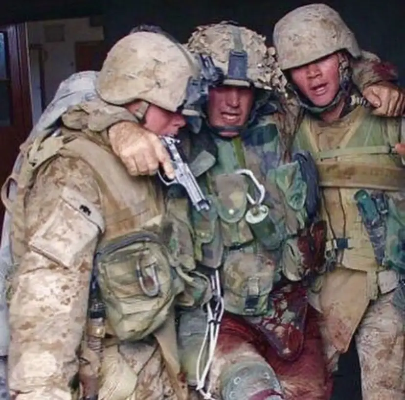 This photograph shows a wounded and bloody 1st Sgt. Kasal emerging from a building in Fallujah, Iraq, in 2004 supported by Marines on his right and left. Then a first sergeant, Kasal had sustained wounds from seven bullets and taken more than 43 pieces of grenade shrapnel during a firefight.  He reportedly had lost 60 percent of his blood by the time he emerged from the house, supported by two lance corporals, but still brandishing his sidearm and Ka-Bar knife. In 2006, Kasal would receive the Navy Cross, the military's second-highest award for valor, for his heroism that day.  According to his medal citation, Kasal had rolled on top of a wounded Marine to shield him, absorbing the shrapnel from an enemy grenade with his own body. 