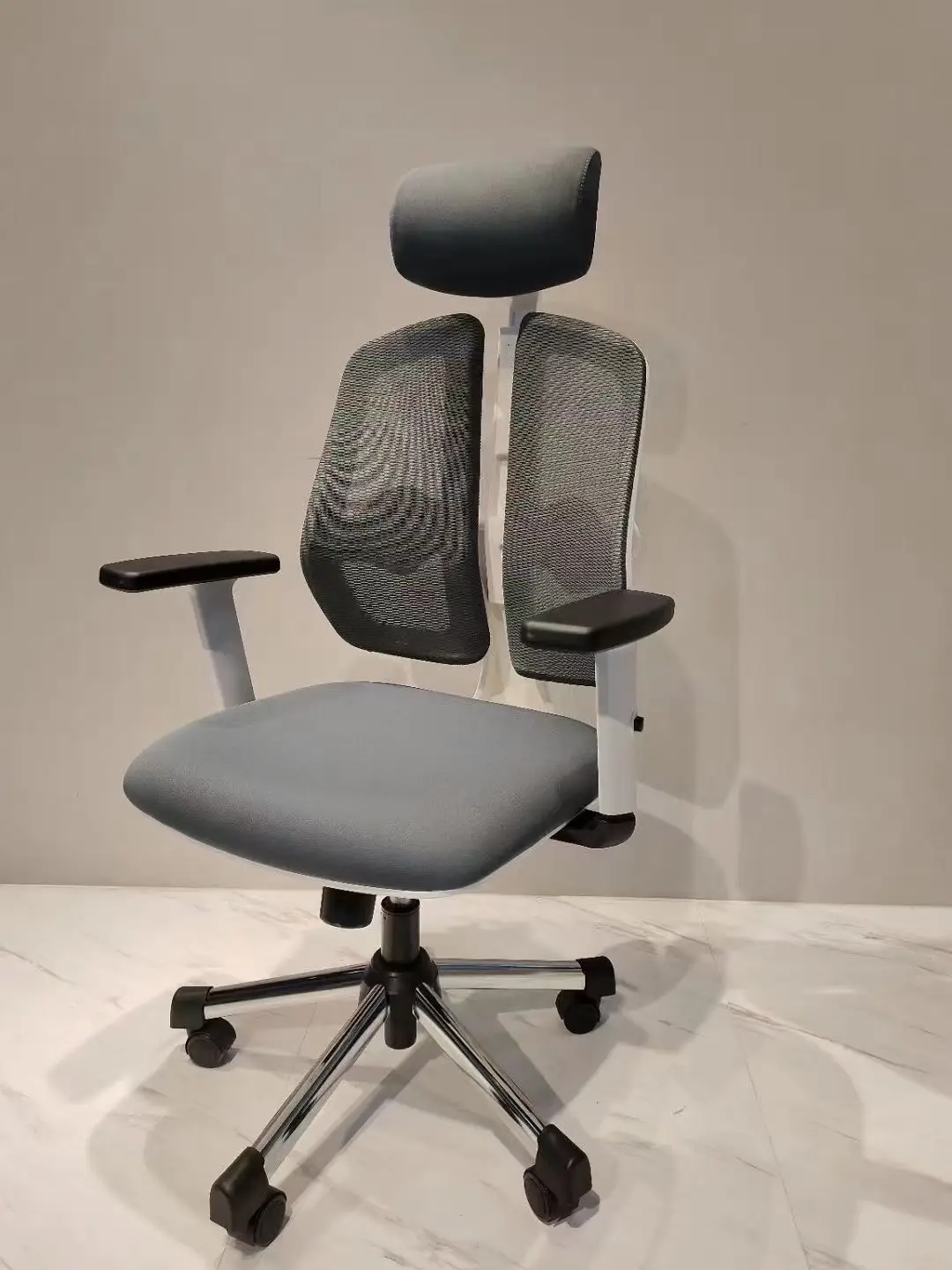 - **Ergonomic Design**: Dual mesh backrest sections provide superior lumbar support, ensuring comfort during long hours of sitting. - **Adjustable Headrest**: Cushioned headrest offers additional neck support, reducing strain and promoting better posture. - **Comfortable Seating**: Padded grey fabric seat designed for maximum comfort, perfect for prolonged use. - **Durable Armrests**: Sturdy black armrests with white support frames enhance stability and offer ergonomic support for your arms. - **Sturdy Base**: Five-star chrome base with smooth-rolling black caster wheels ensures durability and easy mobility. - **Sleek Aesthetic**: Modern and stylish design fits seamlessly into any office or home workspace, enhancing the overall decor. #ergonomicchair #importfromchina 