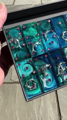 Available for sale. Latest petri charm inclusion project - who doesn’t love 🐬🐬🐬. Demolded last night but waited for my lunch break in the sunshine to photograph. SO pretty. I must be mad. Trying to achieve 28 tiles which all have petri effect and match in palette. Semi transparent tiles are drawn from a bag. Gives the artist a LOT of imagination for design. 🫣🫣🎨🎨🐇🐇#holowaypetri #houseofthewhiterabbit #teexpertcrystalclear #teexpertresin #claireholoway #resinjewellery 