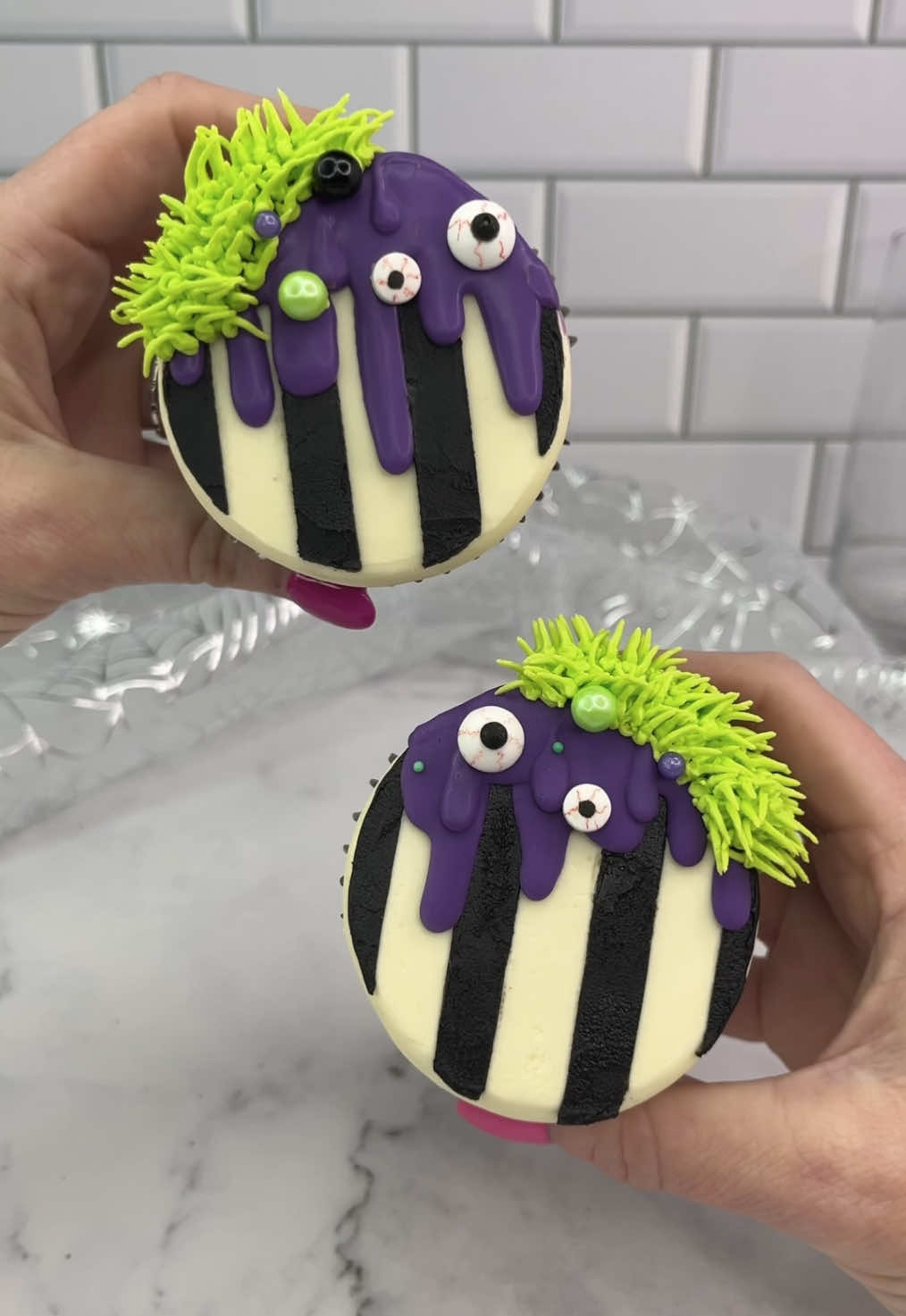 Beetlejuice Beetlejuice 🖤🤍 Beetlejuice inspired cupcakes 💚💜 🖤 Pipe white buttercream onto a cupcake. 🤍 Press it flat into parchment paper. 🖤 Freeze for 20 minutes. 🤍 Remover from paper. 🖤 Add thin parchment strips to the top.  🤍 Spread black buttercream over the top. 🖤 Peel off the strips. 🤍 Add a purple chocolate drip and green buttercream to the edge (using tip 233) decorate with candy eyes 👀 and sprinkles. #beetlejuice #cupcakedecorating #cakedbyrach #cupcake #halloweenbaking #cakeart #beetlejuice2 #spookytreats 