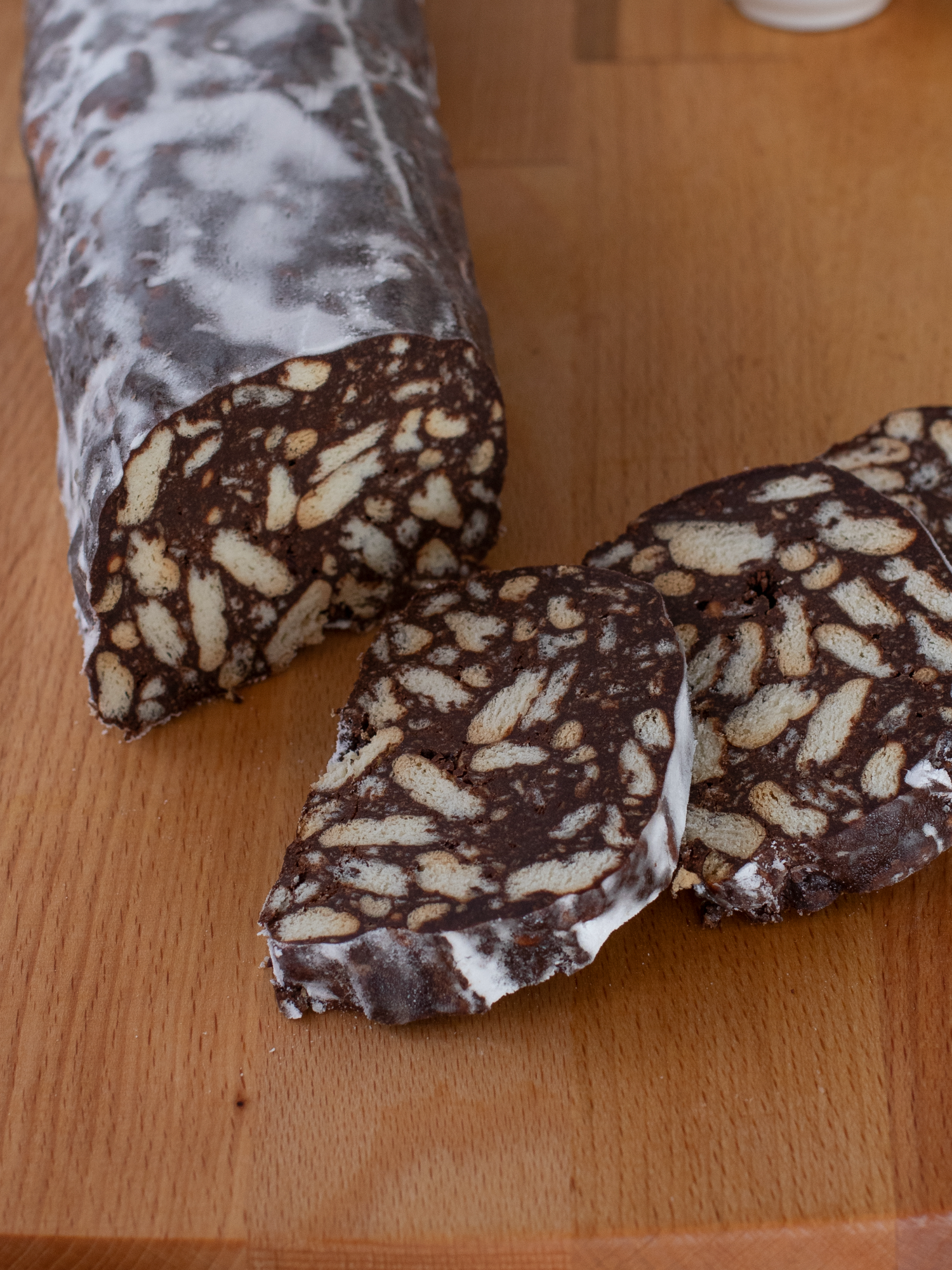 SALAME DI CIOCCOLATO ANNI ’80 Un dolce senza cottura e senza uova molto semplice da realizzare, che piacerà di sicuro a tutti! INGREDIENTI per 2 salami 500 g di biscotti secchi 150 g di zucchero 50g di cacao amaro 200 ml di latte 150g di burro 100g di granella di nocciole (opzionale) PROCEDIMENTO: Iniziamo preparando la glassa: in una ciotola mescoliamo lo zucchero con il cacao amaro, mescolando fino ad amalgamare bene gli ingredienti e mettiamo da parte. In un pentolino, facciamo sciogliere il burro con il latte. Una volta che il burro sarà completamente fuso, versiamolo sul mix di zucchero e cacao e mescoliamo. A parte spezzettiamo grossolanamente i biscotti e versiamo la glassa al cioccolato sopra di essi, aggiungendo anche le nocciole. Mescoliamo e schiacciamo il tutto con una spatola per distribuire bene gli ingredienti. Prendiamo un foglio di carta forno e versiamo una parte del composto, dandogli la forma di un salame. Arrotoliamo bene la carta intorno al salame e chiudiamo le estremità come una caramella. Ripetiamo il procedimento per gli altri salami e mettiamo tutto in frigorifero per almeno 2 ore. Trascorso il tempo, tiriamo fuori i salami e cospargiamoli con zucchero a velo prima di tagliarli a fette. Il salame di cioccolata va conservato in frigorifero e rimane ottimo per diversi giorni. Avvolgiamolo nella pellicola trasparente o nella carta forno per evitare che assorba umidità.   #salamedicioccolato #senzauova #dolcicioccolato #fattoincasadabenedetta #benedettarossi #ricetta #ricettafacile