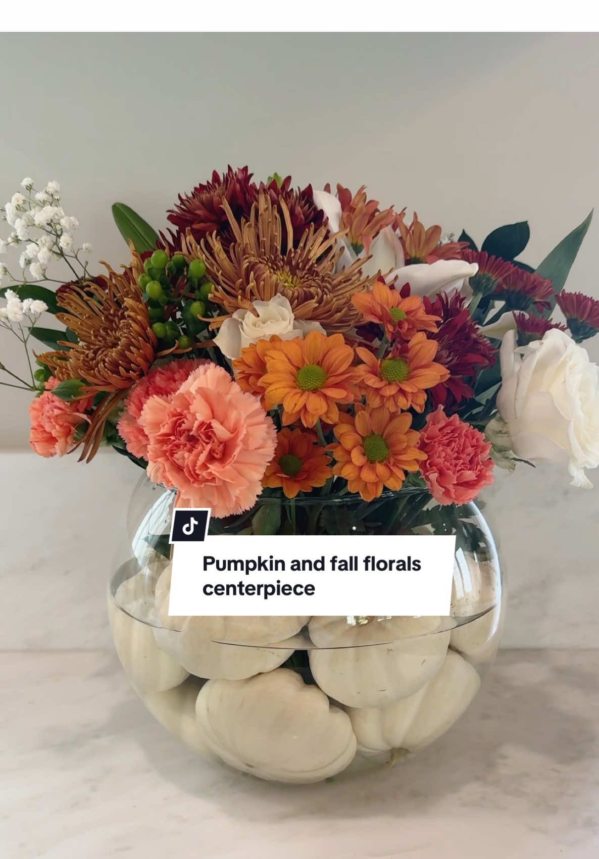 Here is an easy and fun way to incorporate your fall florals and pumpkins into a centerpiece. Grab a large round vase and fill it half way up  with water. Add your mini pumpkins and then add your florals!! Perfect for your thanksgiving table or just to have out on your counter this fall season! #fall #thanksgiving #thanksgivingtablescape #fallflorals #falldecorideas #diyideas #diyhomedecor #cozydecor #pumpkins 