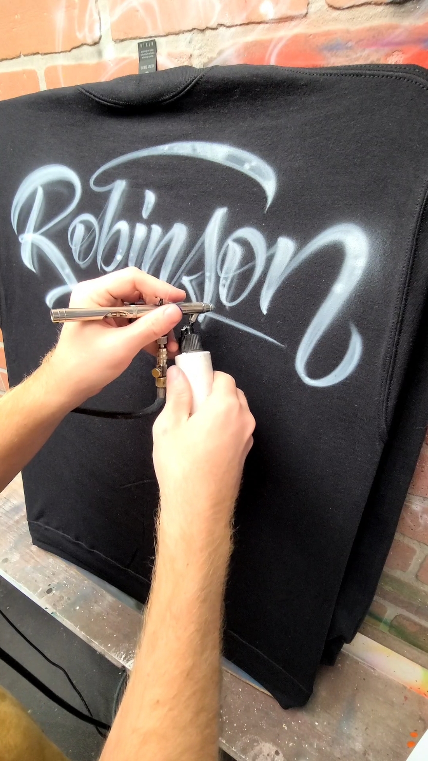 Yesterday I airbrushed a simple calligraphy design on a black sweater. Yes, painting on black items is possible, and it looks great! The only thing is, it takes much longer, and many coats of paint. this can be a pain, especially for detailed artworks. painting on black will take 2-3 times longer,  and has to cost that much more as well.  #airbrush #graffiti #art #design #calligraphy #tattoo #custom #script #handlettering