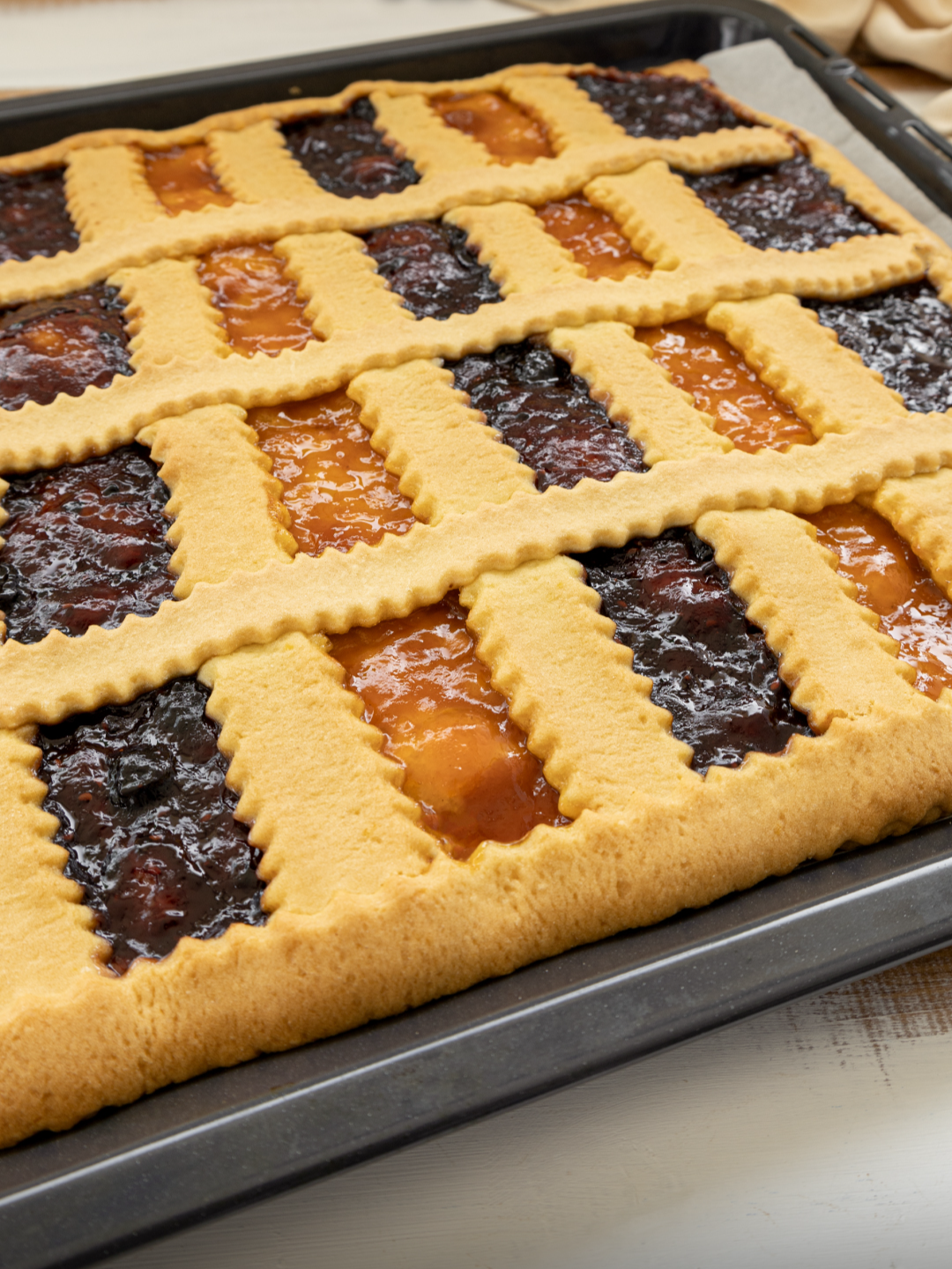 CROSTATA XXL SENZA STAMPO  Una ricetta semplicissima per una crostata alla marmellata, ideale per la colazione, la merenda o per arricchire un buffet. INGREDIENTI PER LA PASTA FROLLA 4 uova 200g di zucchero 160g di olio di semi La scorza grattugiata di 1 limone 16g di lievito per dolci 650g di farina PER LA FARCITURA 200g di marmellata ai frutti di bosco 200g di marmellata di pesche PROCEDIMENTO Per prima cosa prepariamo la frolla: in una ciotola rompiamo le uova e aggiungiamo lo zucchero. Mettiamo anche il lievito, la scorza di limone grattugiata e l’olio. Iniziamo a mescolare con le mani (o se preferiamo con una forchetta). Aggiungiamo la farina poca alla volta, continuando a mescolare per incorporarla. Quando l’impasto ha preso consistenza, spostiamolo sul piano di lavoro infarinato e continuiamo a lavorarlo fino a ottenere un risultato liscio e omogeneo. Una volta pronta la frolla (non dovrà più attaccarsi alle dita) teniamola da parte sul piano infarinato. Poi prendiamo la placca del forno e tagliamo un foglio di carta forno a sua misura. Stendiamo tre quarti della frolla sul foglio di carta forno infarinato, tenendo il resto per la decorazione. Infariniamola e allarghiamola prima con le mani. Ora stendiamola con il mattarello fino a formare un rettangolo grande come la carta forno, arrivando a uno spessore di circa mezzo cm. Riprendiamo la placca del forno e facciamo scivolare dentro la base di frolla. Ora possiamo farcire la crostata: aiutandoci con due cucchiai sistemiamo le due marmellate sulla base alternando i due gusti e creando quindi delle strisce di due colori diversi. Mettiamo da parte la base farcita e stendiamo il resto della pasta frolla, sempre aiutandoci con farina e mattarello. Facciamo un rettangolo non troppo preciso. A questo punto con una rotella dentata ricaviamo tante strisce larghe circa 1,5 cm ciascuna. Decoriamo la crostata sistemando le strisce di frolla sia nel punto di contatto tra le diverse strisce di marmellate, sia a incrociare, creando quindi una griglia. Concludiamo facendo la cornice esterna con alcune strisce di frolla. Infine sigilliamo bene i bordi premendo con le dita e inforniamo in forno preriscaldato ventilato a 170 °C per 25-30 minuti (col forno statico aumentiamo la temperatura di 10 gradi). Ed ecco pronta la nostra crostata xxl senza stampo, friabile, colorata e golosissima. Lasciamola intiepidire un po’ e poi tagliamola a quadrotti per gustarla! #crostata #crostataallamarmellata #Recipe #ricettafacile #benedettarossi #fattoincasadabenedetta #cucinaitaliana