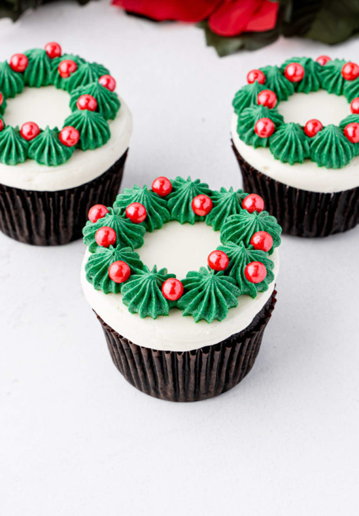 🎄Christmas cupcake series | Cupcake 2 - Wreath cupcakes! Simple and adorable, these wreath cupcakes only require Wilton 1A and Wilton 4B piping tips and green and white buttercream (with some red sugar pearls, of course)! Find the full tutorial on cakemehometonight.com! #christmascupcakes #cupcakedecorating #cupcakes #christmaswreath #wreath 