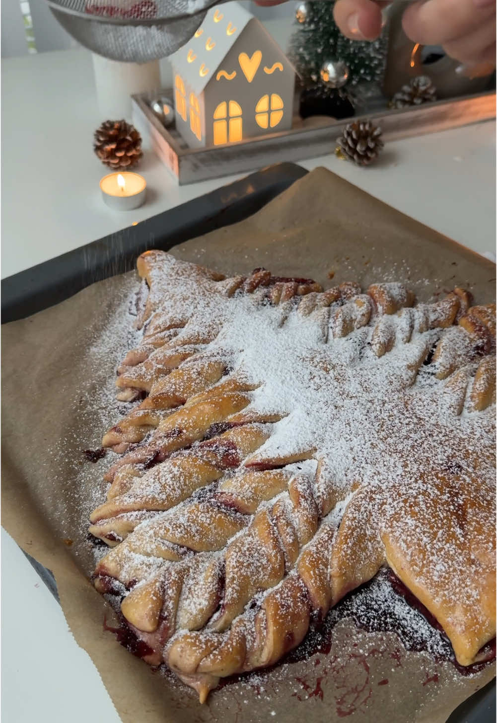 Christmas tree-shaped cherry bun❄️🍒 Ingredients: 320 ml warm milk 60g sugar 8g dry yeast  1 egg (room temperature) 60g melted butter (NOT hot) 550g all purpose flour  In a big bowl mix together warm milk, sugar and yeast. Let it sit for 10 minutes. Add one medium egg room temperature and melted butter (make sure it’s not hot bc yeast could die & your dough wouldn’t rise), mix well with a spoon.  Knead the dough by folding it into a ball. Add some more flour if it’s way too sticky.  The dough should be sticky a little but not very liquid. Let it proof for 1 hour in a warm place. For the cherry filling: Boil 300g frozen cherries with 2 tbs sugar and 100ml water for 15-20 minutes. The texture should be jam-like and the water should mostly evaporate. If it’s too liquid add 1 tbs starch (1 tbs starch mix with a 2 tbs water and then add to cherries to there are no starch clumps). Divide the dough into halves. Roll one half into a circle and add your filling. Roll another half and cover with it the first one.  Cut the form of a tree like I showed in the video and then cut into small lines creating “branches” of a tree.  Sprinkle with beaten egg and bake in the preheated to 180C oven 35-40 minutes or until golden brown. Sprinkle with powdered sugar after baking but it’s optional.  #christmasrecipe #christmasbaking #christmastok #bakingrecipe #christmasbakingideas #winterbaking 