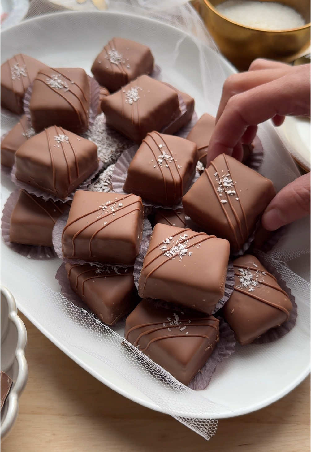 Todays Kitchen: EASY BOUNTY BONBONS - ONLY 5 INGREDIENTS #5ingredients #chocolate #bonbon #bounty #Recipe #food #fy #fyp #foryoupage CREAM ▫️250 g mascarpone   ▫️200 g white chocolate   ▫️100 g grated coconut   FILLING   ▫️30 ml heavy cream   ▫️100 g milk chocolate   ▫️5 g grated coconut   COATING ▫️250 g milk chocolate   GARNISH ▫️grated  coconut   Melt the white chocolate using a double boiler and let it cool slightly.   Place the mascarpone in a bowl and mix it with the cooled white chocolate. Add the grated coconut and stir well.   Heat the cream until just below boiling. Add the milk chocolate, let it sit for 1 minute, then stir until smooth and creamy. Let the ganache cool completely.   Transfer the chocolate ganache to a piping bag.   Spread half of the coconut mixture evenly over the bottom of a pan. Pipe a layer of chocolate ganache over the coconut mixture and sprinkle with grated coconut. Spoon the remaining coconut mixture on top and smooth the surface using cling film. Place the pan in the freezer for 2–3 hours or let it set overnight.   Remove the set coconut cake from the freezer and cut it into equal-sized squares.   Melt the milk chocolate (250 g) using a double boiler.   Dip each square into the melted milk chocolate.   Place them on a sheet of baking paper. Garnish by drizzling fine lines of chocolate over the top and optionally sprinkle with extra grated coconut. Let the chocolate harden completely. TIPS: Let the mascarpone come to room temperature before mixing it with the white chocolate. This prevents lumps and makes it easier to combine. Line your baking pan with parchment paper before adding the coconut mixture. This makes it easier to remove the bars from the pan. Use a sharp knife, warmed under hot water and dried, before cutting the bars. For an extra festive look, you can also use chopped nuts, colorful sugar sprinkles, or a touch of edible gold dust instead of just shredded coconut. I used a baking pan with dimensions of 30 x 13 cm. TIME Prep time: 20-30 minutes Cooling time: At least 2-3 hours Total time: Approximately 3.5 hours