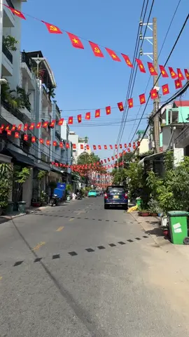 The street is decorated with rows of red flags bearing the symbols of Vietnam and the Communist Party, flanked by buildings and lush greenery under a clear blue sky 🇻🇳☀️❤️🎉 #saigon #vietnam #tetnguyendan2025🧧🎆🧨  #xuhuong 