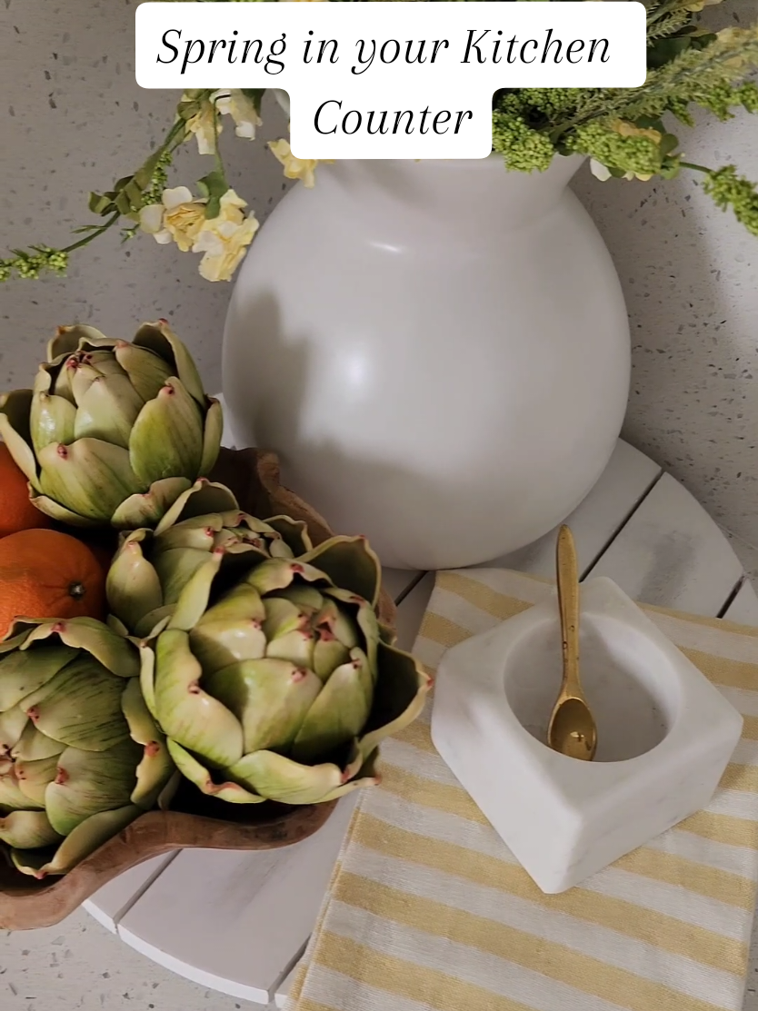 Spring is all about bringing fresh energy and bright colors into your home, and your kitchen is the perfect place to start!  I styled this corner with a simple tray, vibrant yellow flowers, a marble salt container, and a pop of orange tangerine for that fresh spring feel. A striped towel and faux artichokes complete the look! Want to shop these pieces and more? Check out my LTK for all the details and where to find them!  #springdecor #kitchendecor #farmhousekitchen #ltk #farmhousekitchen #whitekitchen #traydecor #amazonfinds #walmartfinds #homestyling #homerefresh  #kitcheninspo 