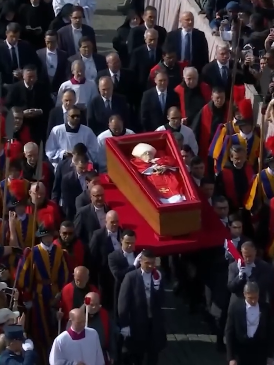 Pope Francis' body was transferred from Casa Santa Marta to St. Peter's Basilica on April 23, 2025, in a solemn procession led by Cardinal Kevin Farrell. The coffin was carried by pallbearers through Vatican grounds, passing under the Arch of the Bells into St. Peter's Square, where over 20,000 mourners gathered. Swiss Guards flanked the procession as church bells tolled and crowds applauded the late pontiff's final journey. The body lies in state at the basilica until his April 26 funeral, with public viewing available until Friday evening. The coffin rests on the main altar rather than an elevated bier per Francis' wishes. Cardinals and clergy paid respects during a Liturgy of the Word service at the Altar of the Confession. #popefrancis 