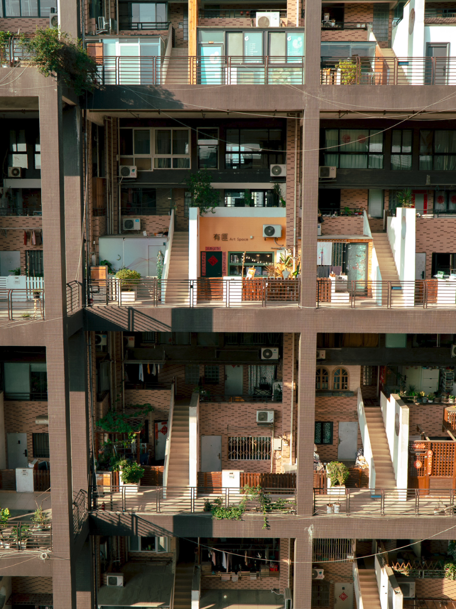 Shots in golden hour that give me hints about lives I've never lived. Photographing Chengdu's architecturally fascinating 'dollhouse' apartments was a bit of a journey! With very little information to go off, save for its name (Manhattan Nature), we took a Didi to the location. However, the apartments are actually hidden within an inner courtyard that is a little ways off from where you would be dropped off on the map. Very few local residents seemed to know what we were talking about even when I showed them the videos, and we actually went around in circles in the area before finally finding it.  Unlike what appeared in the photos, where I thought I saw some cafes and commercial areas, the buildings are predominantly residential and we were the only tourists there. We couldn't really figure out how to get up to the Manhattan Nature apartments themselves without an invitation as there is building security there, and got lucky to enter the opposite building because a passing resident kindly let us up to the upper floors floors there, where there was a common space to look across the courtyard and see the iconic angle of all the apartments laid out in front of you.  I think this is a beautiful piece of modern architecture, allowing people the luxury of a double height apartment and also giving them space in 'front' of their living quarters to have a courtyard, facade, greenery and make each allotment feel more private and house-like. It was fascinating to see the different ways people chose to utilise the space and I would love to see this influence brought into more housing design, such as in Australia.   While very lucky to have gotten a few shots in golden hour, this definitely isn't your regular tourist attraction so I would visit with caution and be respectful of the peace of the residents.  Tried a new photo editing style inspired by @jamtuna's dramatic filmic chiaroscuro 🤌🏻✨ #chengdu #chinatravel #architecture #成都 #中国旅游 #中国 