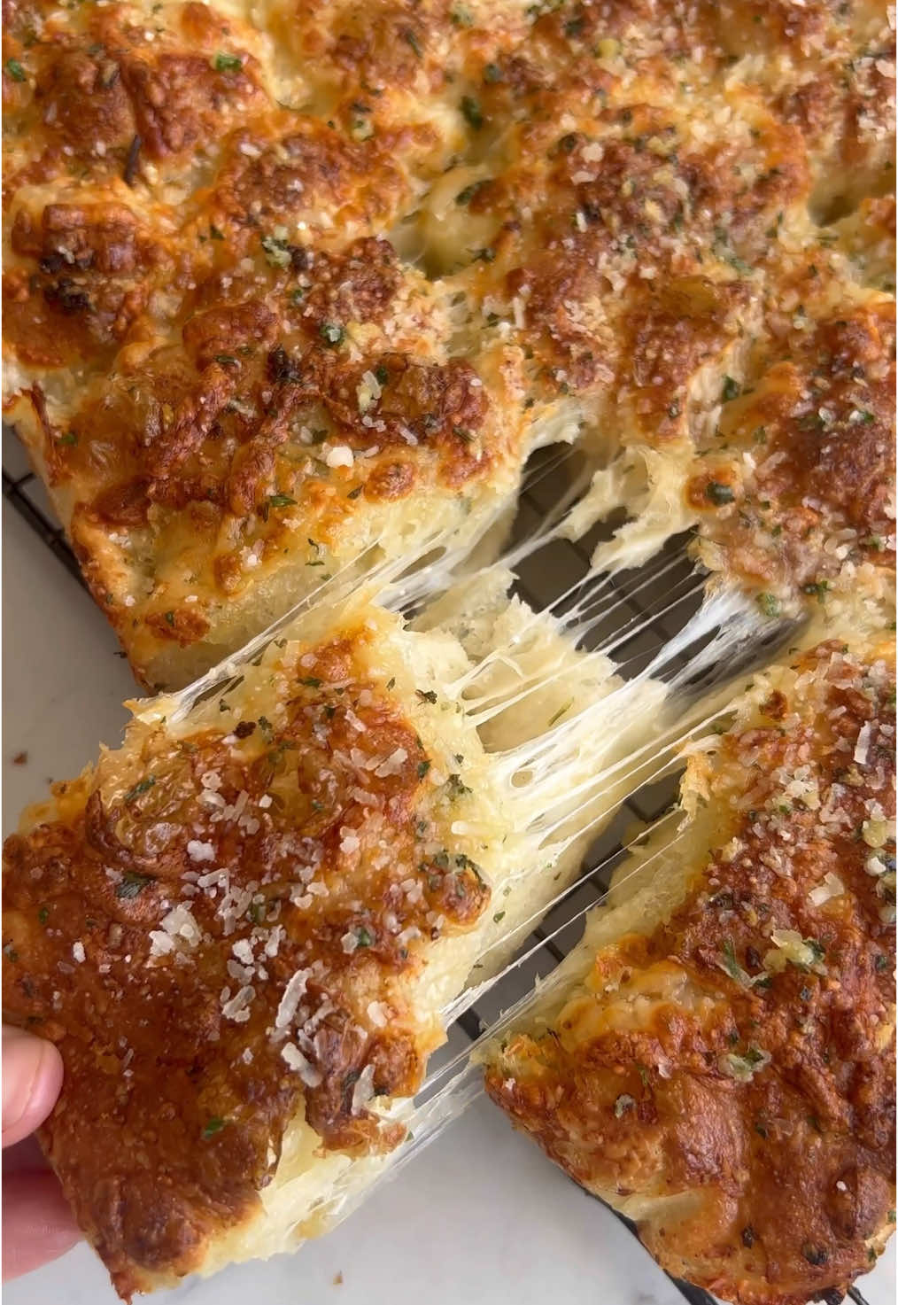 Garlic Butter + Cheese Pull-Apart Focaccia Rolls 🧄  Ingredients 1 batch same-day focaccia dough (this can be found on page 22 in my cookbook or pinned at the top of my page here) 115g (1/2 cup) garlic butter, grated and frozen  125g (1.25 cups) low-moisture mozzarella cheese, grated 40g (1/2 cup) finely grated Parmesan 90g (6 tablespoons) salted butter  5-6 cloves garlic, finely minced 1 teaspoon dried garlic granules  1.5 tablespoons parsley, finely chopped  Mix up a batch of same-day focaccia dough. Incorporate the the frozen grated garlic butter during the   stretch and folds - scatter one half of the grated garlic butter over the dough for the first stretch and fold and fold it in, wait 15 minutes and repeat with the second half of the grated garlic butter (keep it in the freezer between folds). Leave to rest at room temperature for 1-1.5 hours. In a small frying pan, melt together the salted butter, minced garlic, and garlic granules over a medium heat. Simmer for 1-2 minutes and then stir in the chopped parsley. On a clean worktop, brush some of the garlic butter into the size of your baking tray (roughly 9x13 inches or 23x33 cm). Tip the dough onto the butter and use buttered fingers to gently pull the dough into a 9x13 rectangle with an even thickness. Rub a little butter onto the edge of a dough scraper or sharp knife and cut the dough into 15 pieces (as evenly sized as possible) by cutting the dough into 3 rows, and then into 5 rows.  Coat each piece with the garlic butter and place into the tray (lined with nonstick parchment) in a 3x5 formation. Be sure to save a small amount of garlic butter to brush over the top once it’s baked. Cover and proof at room temperature for 1-1.5 hours. Scatter half the grated mozzarella and half the grated Parmesan over the dough. Dimple. Bake on lowest rack of oven at 220C/430F for 12 minutes. Remove from oven and sprinkle over the remaining cheese (reserving a couple of tablespoons of the Parmesan for garnish). Return to oven to finish baking for another 8-10 minutes, or until golden.  Brush over the remaining garlic butter and scatter over the reserved Parmesan cheese. Pull apart into rolls and enjoy warm!  Inspired by @Amy Coyne | Sourdough Recipes viral croissant bread method #focaccia #garlicbread #breadtok #dinnerrollrecipe #focacciatok #pullapartbread #breadmaking 