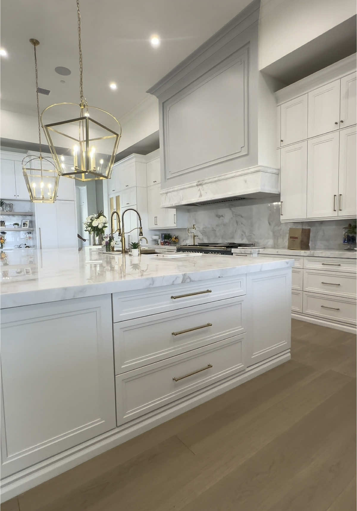 Golden hour meets golden hardware ✨ This kitchen at our #PaintedMountain project is the perfect blend of elegance and function. From the oversized island with mitered stone countertops to the custom cabinetry and polished brass fixtures, every detail was thoughtfully designed. The soft wood floors ground the space while those statement pendants bring it all together.  #HomeGymGoals #LuxuryLiving #PaintedMountain #PickleballCourt #HomeBasketballCourt #AFTConstruction