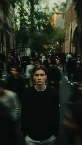 Prompt : Cinematic portrait of a young man standing still in the middle of a busy urban street. He wears a dark oversized sweater, looking straight at the camera with a calm expression. Motion-blurred crowd rushes past him from all sides, emphasizing contrast between stillness and chaos. Moody lighting with soft shadows, 35mm film look, shallow depth of field, sharp focus on subject, background in soft blur. Portrait aspect ratio 4:3.