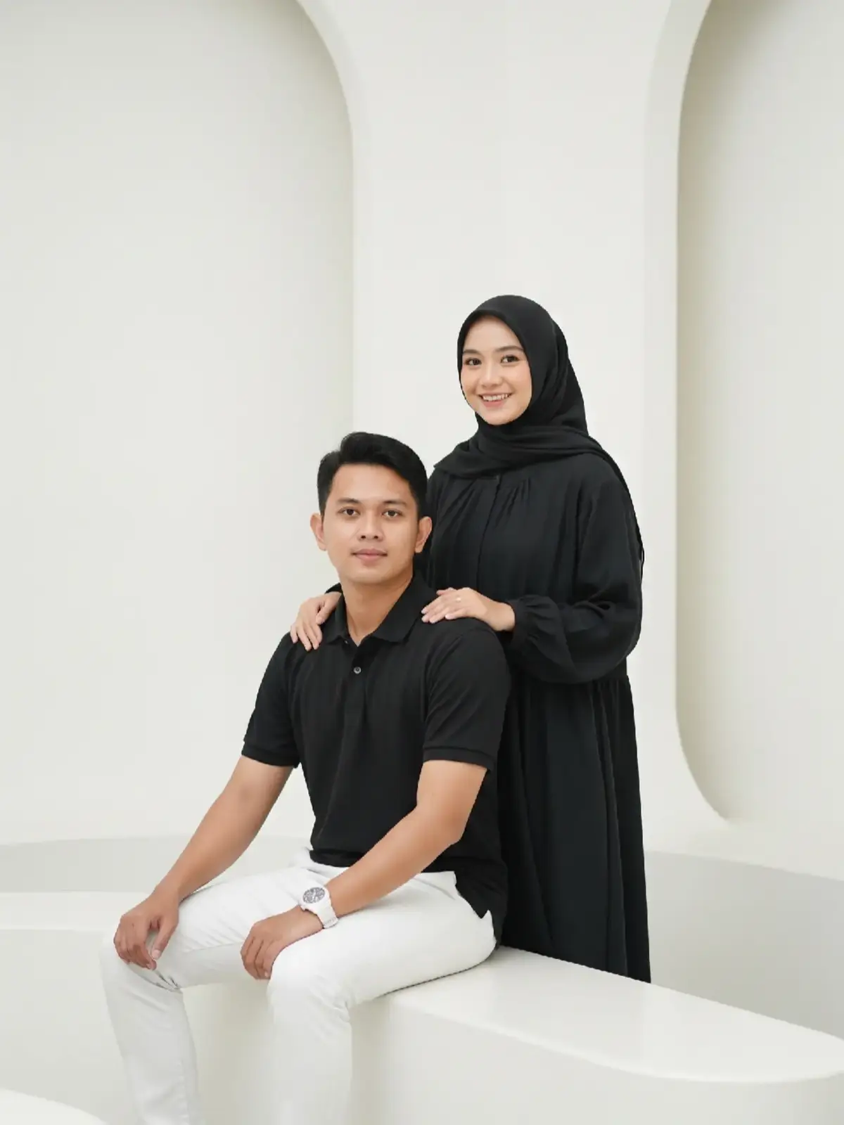 Prompt:  Pasangan muda Indonesia bergaya modern minimalis sedang berfoto di dalam ruangan bernuansa putih bersih dengan pencahayaan natural. Pria duduk di bangku dengan mengenakan outfit: kaos polo hitam, celana panjang putih, dan jam tangan putih sporty. Wanita berdiri di belakangnya dengan senyum hangat, mengenakan gamis hitam longgar dan hijab hitam simpel, menciptakan kesan elegan dan kalem. Komposisi simetris, latar belakang lengkung putih bersih, rasio foto 9:16, suasana studio modern dan terang, gaya foto formal namun hangat. #fyp #fypage #aiphoto #gemini #ai #beranda 