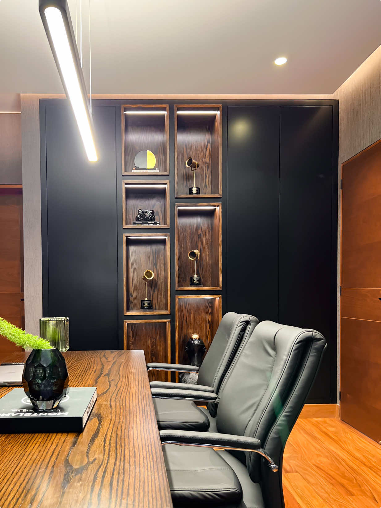 Una oficina en casa también puede ser un lugar de inspiración. Este espacio fue diseñado para reflejar carácter y trayectoria: un escritorio en L enchapado en madera, un estante que exhibe logros con orgullo y una paleta de madera y negro que transmite fuerza y elegancia. La pequeña sala de estar con butacas de cuero invita a la pausa, al pensamiento y a la conversación serena. Un ambiente que combina funcionalidad y significado. #DiseñoInterior #Interiorismo #ArquitecturaInterior #DiseñoDeOficinas #OficinaEnCasa #DianaChoy #ProyectoDC