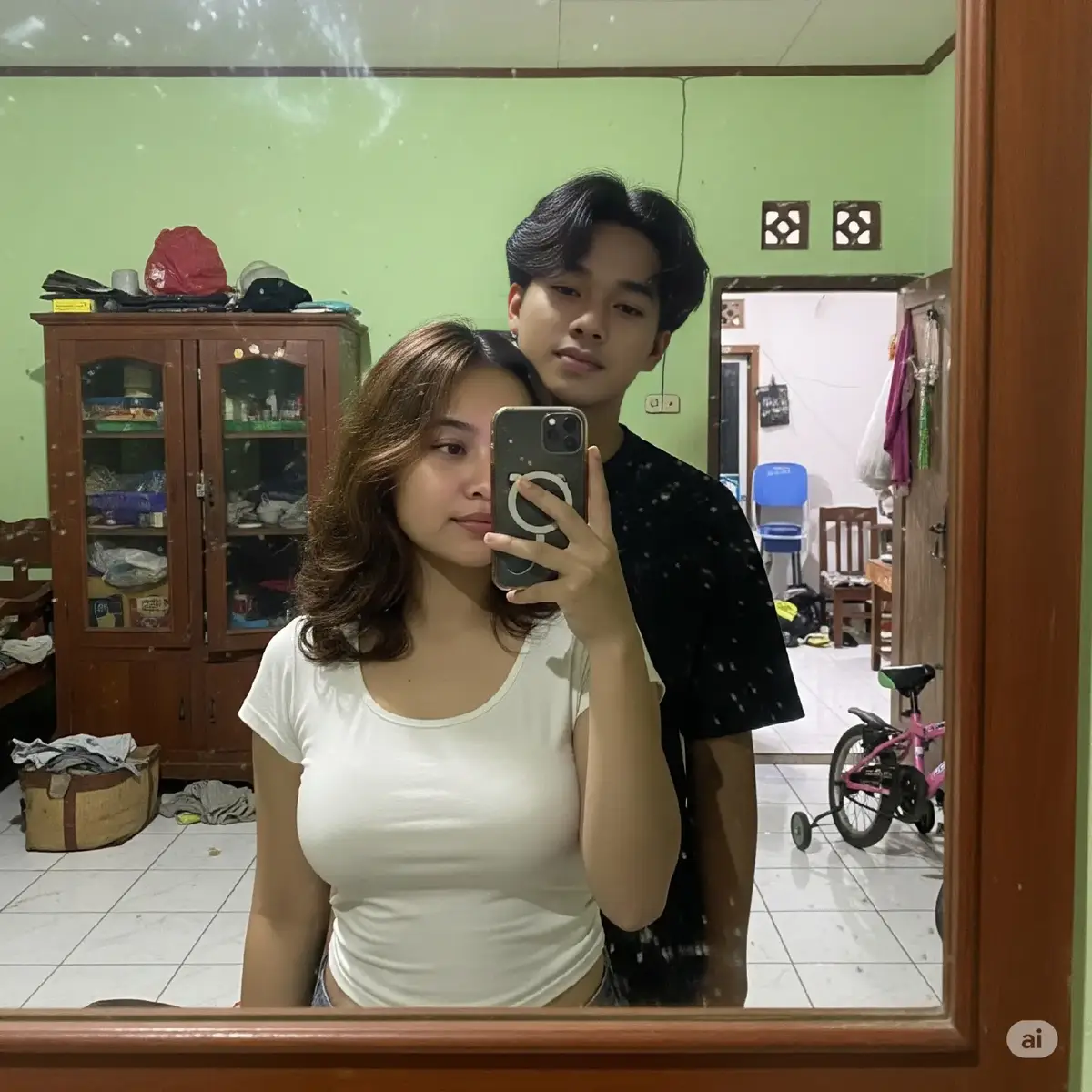 Seorang wanita muda asal Indonesia, berusia 18 tahun, rambut sebahu bergelombang poni rambut menutupi dahi , sedang mengambil selfie di cermin bersama pacarnya asal indonesia berusia 19 tahun dengan ciri-ciri laki-laki tampan dengan rambut agak panjang potongan poni nya pas di atas mata dan memakai baju hitam sedang memegang bahu pasangannya, dalam rumah sederhana khas Indonesia dengan dinding yang dicat hijau. Ia mengenakan baju crop top putih, Ruangan tampak berantakan dan realistis: ada lemari kayu, lantai keramik putih, beberapa pakaian kotor berserakan, sampah kecil seperti bungkus plastik dan potongan kertas di lantai, serta sebuah sepeda anak kecil yang diletakkan di sudut ruangan.  Suasana terasa hangat dan sehari-hari, mencerminkan rumah sederhana khas Indonesia yang penuh kehangatan dan kerendahan hati. Semua detail dibuat sangat realistis: permukaan lemari kayu terlihat memiliki goresan-goresan, cat hijau pada dinding tampak sedikit pudar, dan lantai keramik memantulkan cahaya lembut. Tambahkan bayangan dan pencahayaan alami dari dalam ruangan yang masuk lewat jendela kecil. Fokus pada nuansa khas Indonesia yang autentik—ruangan yang berantakan namun terasa benar-benar dihuni. Mereka berdua terlihat romantis dengan gestur tubuh dan ekspresi wajah yang alami. Hasil foto close up. Tambahkan efek cermin sedikit buram dan banyak noda goresan di permukaannya agar foto terlihat seperti realistis,lots detail. Wajah perempuan terlihat jelas tidak menutupi objek lain. #ai #geminiai  #fyp #prompt 