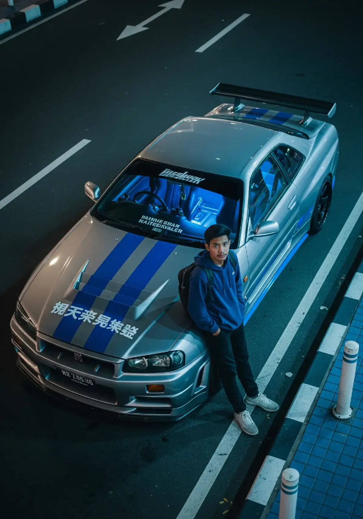1.buka Gemini 2. paste kan prompt. 👇 • Gaya & Suasana Gaya fotorealistik dengan pencahayaan malam hari khas lampu kota Warna dominan: biru neon, abu-abu metalik, dan cahaya jalan Suasana misterius dan urban, bergaya street racing Jepang • Subjek Utama (Manusia) Seorang pria muda khas Indonesia berdiri bersandar di mobil sport Mengenakan hoodie biru gelap, celana gelap, dan sepatu sneakers putih Ransel hitam di punggung, tangan dimasukkan ke kantong Tatapan menatap ke atas ke arah kamera (angle dari atas) • Kendaraan (Mobil Sport) Mobil sport berwarna silver dengan strip biru khas street racing Desain menyerupai Nissan Skyline R34, full body kit Stiker modifikasi dan tulisan Jepang di kap mobil Interior mobil memancarkan cahaya biru dari dalam • Lingkungan Sekitar Lokasi di tepi jalan malam hari, aspal gelap dengan garis putih Trotoar dengan ubin biru dan tiang putih Lampu kota menciptakan nuansa futuristik dan dramatis Cahaya memantul di permukaan mobil, menciptakan efek sinematik • Nuansa Warna & Pencahayaan Pencahayaan redup dengan efek neon biru dan hijau Kontras tinggi antara mobil yang mengkilap dan latar gelap Refleksi lampu jalan di bodi mobil dan aspal basah ukuran foto 3:4 #nissanr34gtr #gtr34 #nissan #nissanr34 #kontenai #gtr34 #geminiai 