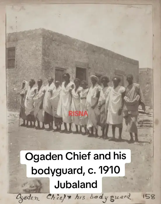 moment frozen in time: an Ogaden elder at the heart of his zareba, his spearmen bodyguards by his side, while a colonial police sentry watches from the background. This powerful photo, taken in Jubaland around 1910, tells a story of Somali leadership under colonial gaze—a time when tradition and empire stood face to face.