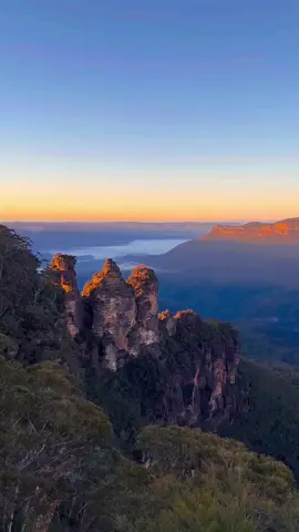 Our famous eucalyptus trees give the Blue Mountains their name and their colour 💙 One hour from Warrane (@Sydney) are the peaks and valleys of the Blue Mountains, home to the striking Three Sisters rock formations ☝️  🎥: IG:parttimeglobetrotting 📍 : Three Sisters, Blue Mountains, @New South Wales  #SeeAustralia #ComeAndSayGDay #FeelNSW #BlueMountains ID: Camera pans across a landscape with three rock pillars in the foreground and a blue hued valley stretching beyond.
