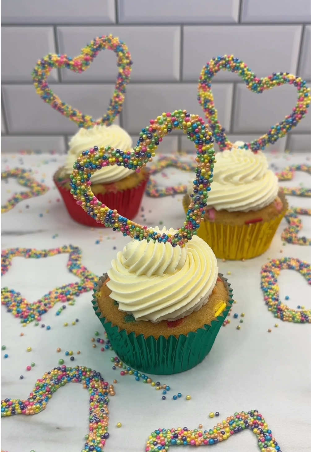 Sprinkle shapes 🌈🧁 Made for @Wilton Cakes  🧁 Melt bright white candy melts in a bowl.  🌈 Line a baking sheet with parchment paper.  🧁 Dip the thicker side of your cookie cutter into the candy melts, shake off any excess.  🌈 Tap the cutter onto the sheet of parchment paper, leaving a candy melts shape.  🧁 Fill the sheet with shapes then pour over the small sprinkles.  🌈 Transfer the tray to the fridge.  Once set, remove the shapes from the paper and keep them in the fridge until ready to use.  🧁 Using white buttercream and tip 8B, add a swirl on top of your cupcakes.  🌈 Sit the sprinkle shape on top of the swirl.  #cakedbyrach #sprinkles #howto #EasyRecipe #bakingideas #cakedecorating 