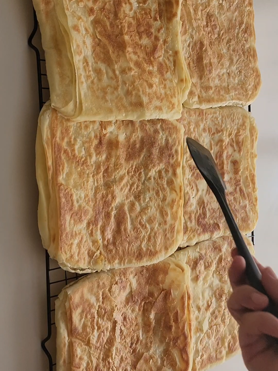 Çıtır Katmer  Çok az malzemeyle bu kadar kolay ve lezzetli 🔥 Tarifi Kaydedip beğenmeyi unutmayın ❤️ Malzemeler 2 su bardağı su (400 ml)  1 tatlı kaşığı tuz (10 gram) 4.5 su bardağı un (540 gram) Yağlamak için 150 gram tereyağı  1 çay bardağı sıvıyağ (100 ml) Kızartmak için  2 yemek kaşığı sıvıyağ   Hamur malzemeleri ile yumuşak ele yapışmayan hamur yoğuruyoruz, hamuru 12 eşit beze yapıp 10 dakika dinlendiriyoruz.  Dinlenen bezeleri servis tabağı büyüklüğünde açıyoruz, diğer yandan eritilmiş tereyağı ve sıvıyağ karıştırıp uygun bir kabı güzelce yağlıyoruz. Açtığınız hamurları yağlanmış kabın içine üst üste koyarak her katına yağ sürüyoruz. Üzerini kapatıp 1 saat dinlenmeye bırakıyoruz.    Dinlenen hamurların hepsini masaya alıp incecik olana kadar elimizle büyütüyoruz, 6 eşit parçaya kesip videodaki gibi katlıyoruz, katladıktan sonra 5 dakikada bu şekilde bekletiyoruz. Hamurları tatlı tabağı büyüklüğünde açıp hazırlıyoruz, kısık ateşte ısıtılmış tavaya çok az sıvıyağla yağlayıp arkalı önlü çevirerek pişiriyoruz. Hepinize afiyet olsun 🫶 #katmer #kahvaltı #kolaytarifler 