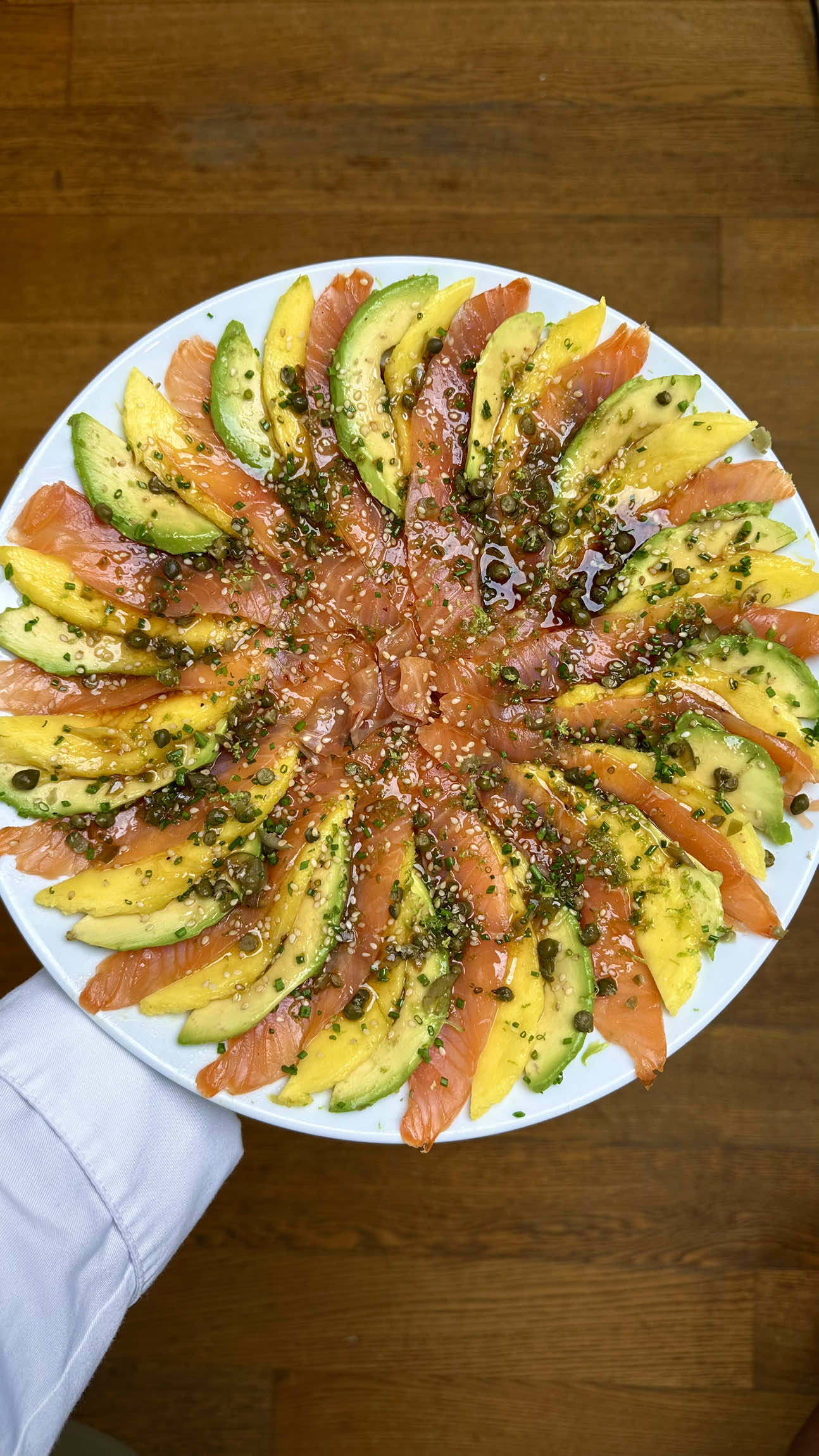 ТИРАДИТО С ЛОСОСЕМ, МАНГО И АВОКАДО 🍣🥭🥑 Свежесть, яркость и нежность в одном блюде. Просто и невероятно вкусно! ⸻ 🥢 Ингредиенты (на 2 порции) 	•	Лосось слабосолёный или свежий sashimi-grade — 200 г 	•	Манго спелое — 1 шт. 	•	Авокадо спелый — 1 шт. 	•	Лук-сибулет — небольшой пучок 	•	Халапеньо — 3–4 тонких слайса 	•	Каперсы — 1 ч. л. 	•	Соевый соус — 2 ст. л. 	•	Оливковое масло — 3 ст. л. 	•	Сок 1 лайма 	•	Цедра лайма — 1 ч. л. 	•	Кунжутное масло — ½ ч. л. 	•	Жареный кунжут — 1 ст. л. ⸻ 👨‍🍳 Приготовление 	1.	Лосось, манго и авокадо нарезать тонкими слайсами. 	2.	Выложить по кругу в порядке: манго — авокадо — лосось, создавая эффект карусели. 	3.	Сверху добавить лук-сибулет, тонкие слайсы халапеньо и каперсы. А также натрите цедру 1 лайма. 	4.	Для маринада смешать соевый соус, оливковое масло, сок лайма, кунжутное масло. 	5.	Полить блюдо заправкой. 	6.	Финально посыпать жареным кунжутом. Приятного аппетита 😋