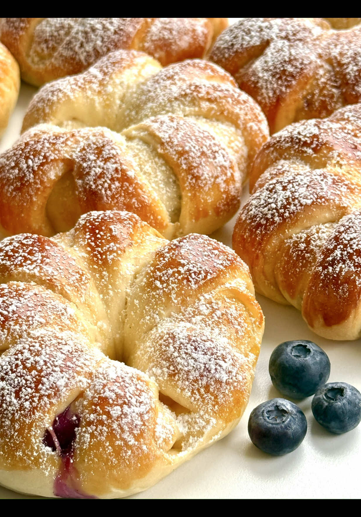 Blueberry Custard Rings Recipe 😍🫐🤍 These yeast-dough rings are not only a real eye-catcher but also an absolute treat. A pastry that is sure to delight everyone – perfect with coffee, for breakfast, or just in between. 🥰 📝 Ingredients (makes about 8 pieces) Yeast Dough 	•	250 g all-purpose flour 	•	1 tsp instant yeast (about 3–4 g) or 10 g fresh yeast 	•	125 ml lukewarm milk 	•	30 g sugar (2 tbsp) 	•	1 egg (size M) 	•	30 g soft butter 	•	1 pinch of salt 	•	1 egg yolk (for brushing) Custard Filling 	•	250 ml milk 	•	40 g sugar (2 tbsp, or to taste) 	•	25 g cornstarch (2 tbsp) 	•	2 egg yolks (M) 	•	1 tsp vanilla extract 	•	50–70 g fresh blueberries 🤍 Instructions 1.	Sift flour into a bowl, make a well, add yeast, a little sugar, and some milk. Let sit 5–10 min until foamy. Add remaining milk, sugar, salt, and half the egg, then knead. Finally, knead in butter until smooth (8–10 min). Cover and let rise 1 h until doubled. 2.	For the custard, whisk milk, sugar, cornstarch, yolks, and vanilla in a saucepan. Bring to a boil, stirring, until thickened. Remove from heat, cover with plastic wrap, let cool, and fill into a piping bag. 3.	Divide dough into 8 balls, roll each into a rectangle. Pipe a custard line along the long side, add 4–5 blueberries. Fold and seal edge. Cut 5–6 slits into the other side, roll up, and shape into a ring, pressing ends together. 4.	Place rings on a tray, cover, and let rest 15–20 min. Brush with egg yolk and bake at 180 °C / 350 °F (top/bottom heat) for 20–25 min until golden. Cool on a rack and dust with powdered sugar. 💡 Extra custard makes a nice dessert in a glass with fresh fruit. Your Blueberry Custard Rings are ready: golden outside, creamy inside, with a fruity surprise. 🫐🤍