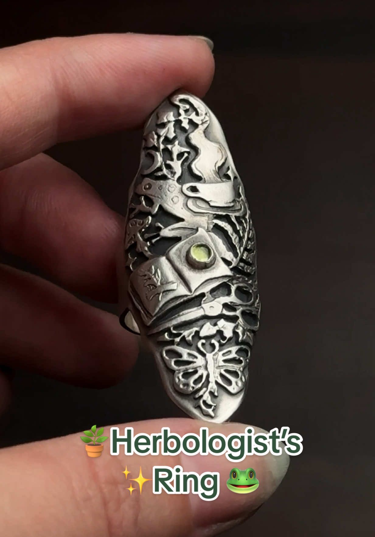 ✨ I’m in my ring-making era! ✨  This design came to me straight from a witchy herbologists book, a gathering of small symbolic objects that together weave a whole story. A frog resting beside a steaming cup filled with a magical herbal tea, ferns curling around an open sketchbook, mushrooms, scissors, butterflies, and at the center, a green peridot gemstone. 🌿💚🐸🪴🔎✂️🧙🏻‍♀️ Size 6 3/4 US  Release date - TBA I’m loving the idea of creating aesthetic imagery in my jewelry, creating wearable collages that capture a mood. Something small enough to wear around your finger, yet layered with meaning, that can tell some much about the person who chooses to wear it.  Fall has arrived for me mentally, anyone else? 🎃🧡👻 #witchyjewelry #witchyaesthetic #fall2025 #witchvibes #jewelrytiktok 