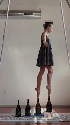Book on Bekah en pointe on bottles on books 😂🖤🩰 next time I need hardback books these are so wobbly! #pointeshoes #ballerina #ballerinasoftiktok #ballettok #enpointebottlewalking 