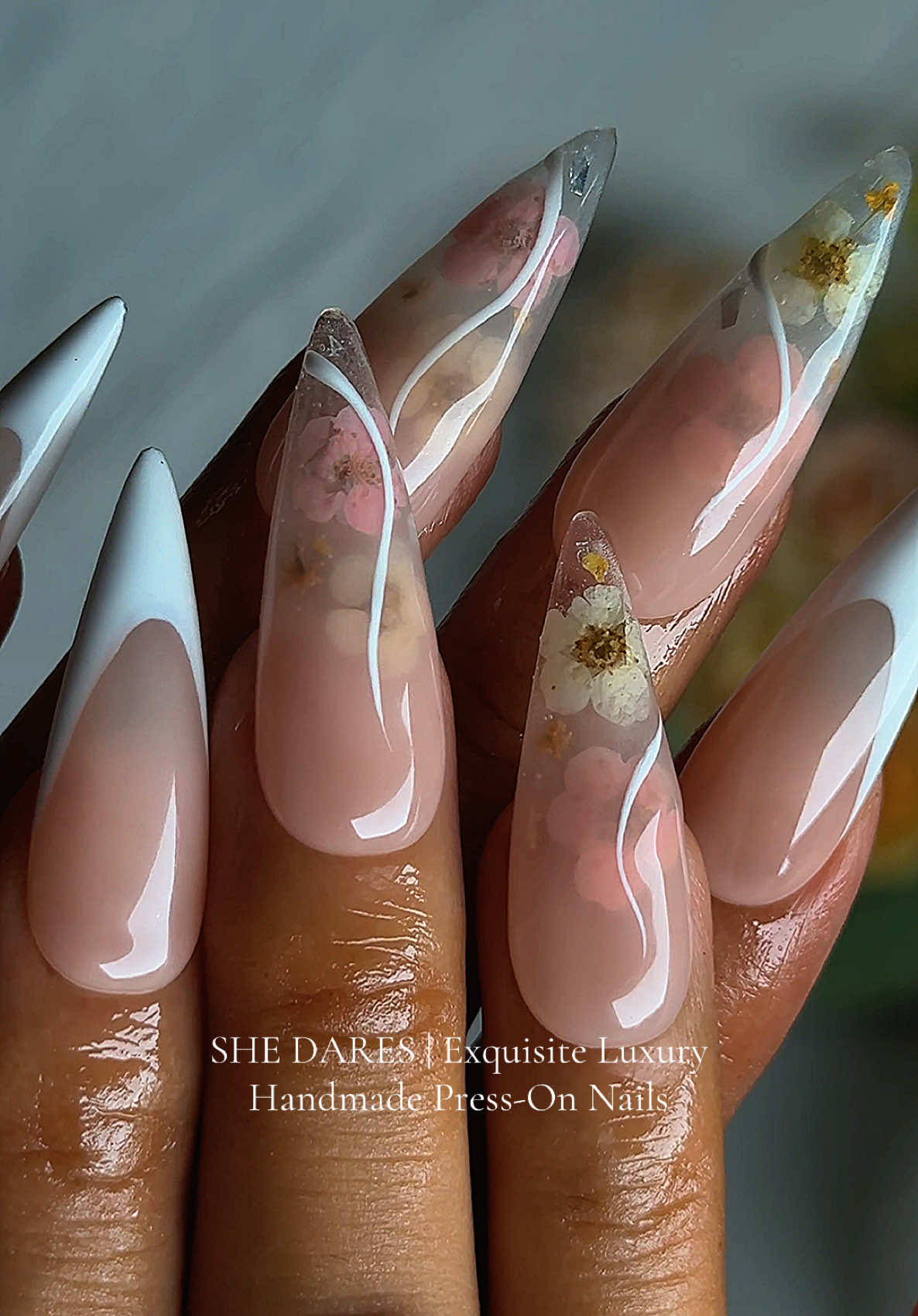 When elegance meets romance 🌸 Sharp French tips with a twist — crystal clear nails kissed with real dried flowers & golden accents. A timeless bridal vibe with a modern edge. 🤍 ✨ Handmade | Reusable | Luxury Press-Ons #SheDares #LuxuryNails #FrenchTips #BridalNails #FlowerNails   
