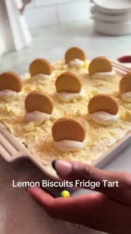 LEMON BISCUIT TART 🍋 I’m trying to find alternatives to the Peppermint Crisp Tart that we all love. I used Lemon Curd to make a lemony cream and lemon-flavoured Tennis biscuits. The chocolate layer is Milky Bar! Yum! Step 1 Whip together the cream layer by whipping 2 cups of Whipping Cream into soft peaks. Then add 1 tin of Condensed Milk and 3/4 cups of Lemon Curd to the whipped cream. Fold together to create a lemony cream, set aside until assembling the tart.  Step 2 Chop 2 large slabs (150g) of Milky Bar Chocolate into small, bite sized pieces. Then set aside until assembling the tart.  Step 3 In a baking tray 20x20 cm, add a small amount of cream to act as a glue. Open 2 packets of Lemon Tennis Biscuits and set aside until assembly.  Step 4 Assemble the tart by placing a layer of tennis biscuits, a layer of cream, a layer of chopped white chocolate. Repeat until you have 3 layers. Then top with leftover cream to create a pillow for the biscuit topping.  Step 5 I placed a Sphere Biscuit on each portion of tart. I created 9 portions so I used 9 lemon cream Sphere Biscuits.  #peppermintcrisptart #nobakedessert #lemonbiscuittart #lemondessert #fridgetart 