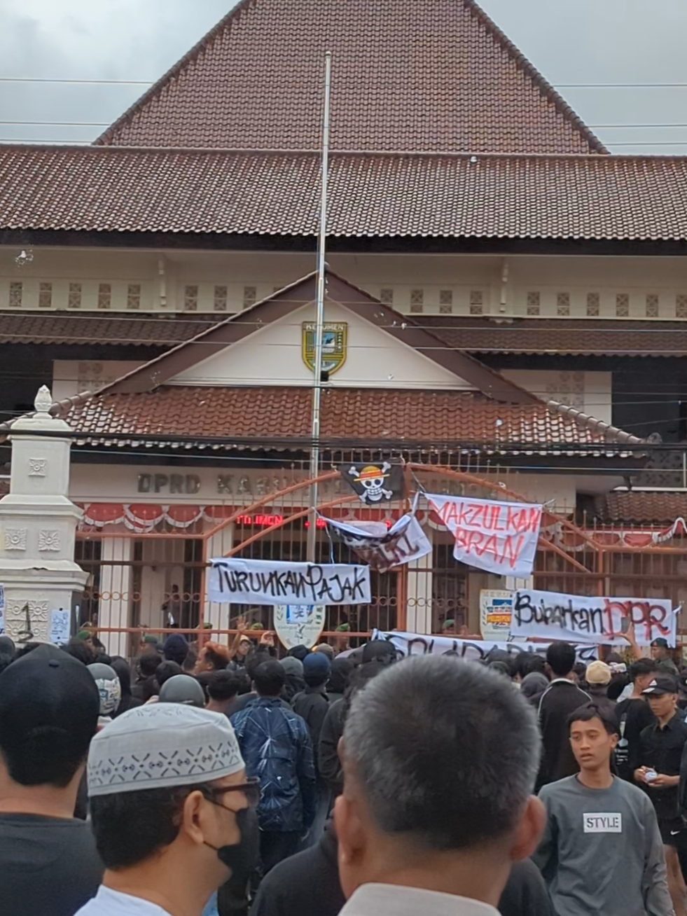 Pantauan di dua lokasi aksi, yaitu Polres dan DPRD Kebumen, menunjukkan perbedaan situasi yang mencolok. Area Polres tampak lengang, sementara di depan Gedung DPRD, sekelompok massa dengan pakaian dominan hitam terlihat sedang melakukan unjuk rasa. Mereka memasang beberapa spanduk di gerbang gedung, dengan tulisan-tulisan seperti “Makzulkan Gibran,” “Turunkan Pajak,” dan “Bubarkan DPR.” Situasi mulai memanas saat massa melempari halaman gedung DPRD dengan batu, botol plastik berisi air, dan bahkan tanaman yang dicabut dari pinggir jalan. Sejumlah aparat TNI terlihat bersiaga di gerbang untuk menjaga keamanan.