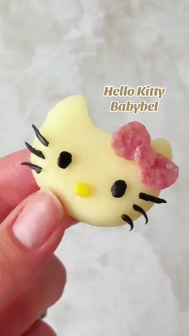 Turning a Babybel cheese into Hello Kitty. Halve your Babybel, then cut the ear shapes with a knife. Make the bow out of salami (shaped with scissors) and use black olives for the eyes and whiskers. Super cute and so much fun to make! #hellokitty #kawaiifood #hellokittyfood #babybel #cheese 