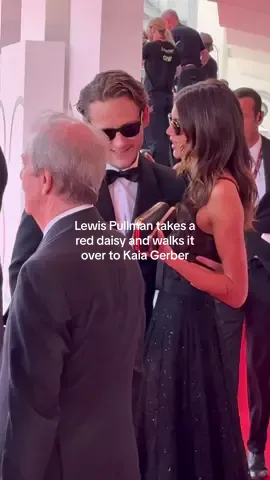 Lewis Pullman takes a red daisy and walks it over to girlfriend Kaia Gerber