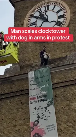 A protester clutching a dog has climbed the clocktower at King’s Cross train station in London. The demonstrator, sitting near a banner that read “Iran belongs to its people” and wearing a black t-shirt emblazoned with the words “no to war”, scaled the structure at around 8am on Tuesday and remained there as of late morning. Firefighters went up in a cherry picker in an attempt to talk the activist down, eventually persuading him to hand over the dog and allow it to be brought to the ground around three hours into the stand-off. Onlookers cheered as the animal came safely down. #news #uk #london #iran 