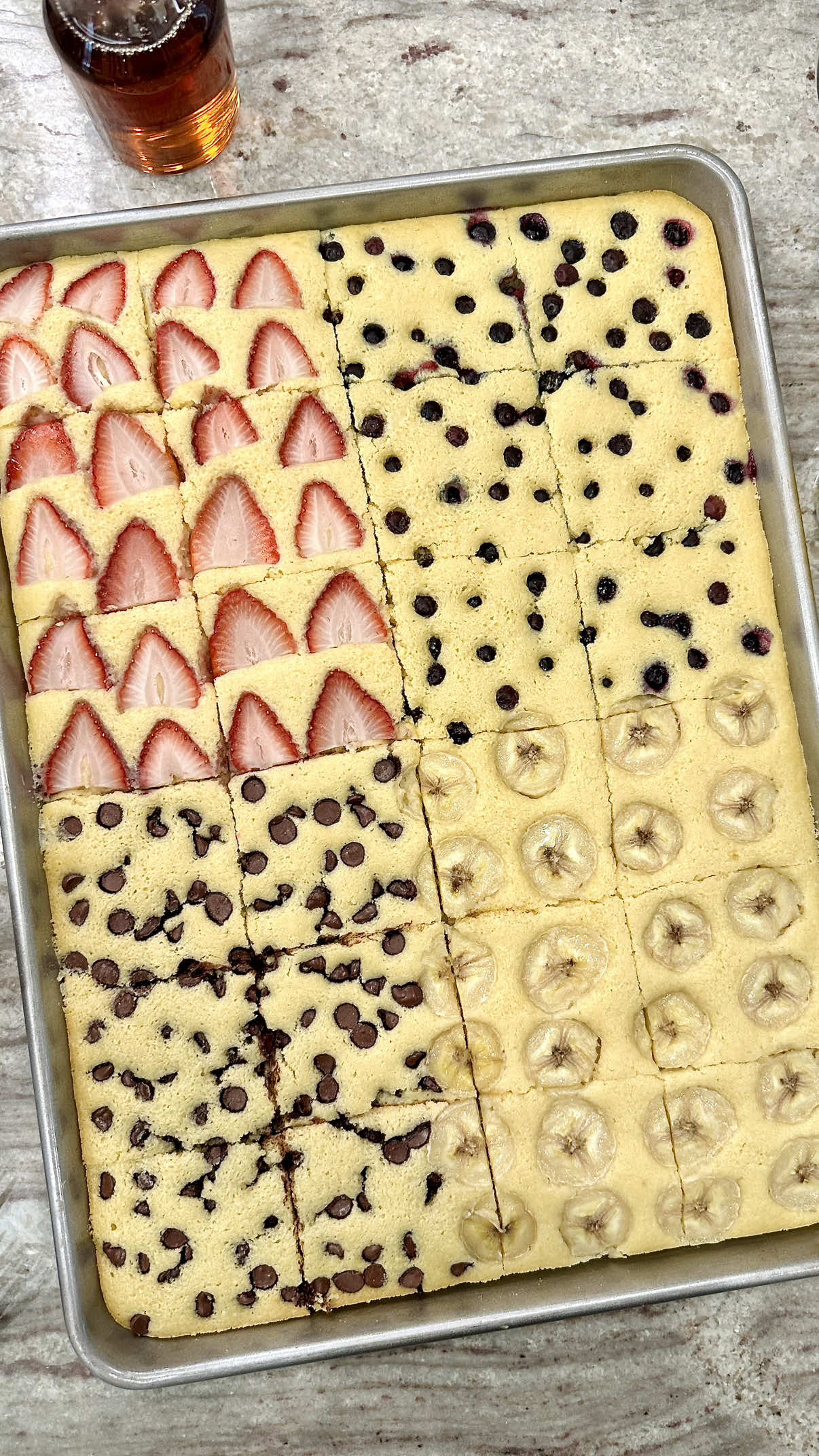 Sheet Pan Pancakes are a staple in our house, and for good reason! They can be made in a matter of minutes and don't slow down our busy morning of sports and school. Pour the batter onto a sheet pan, then right into the oven for the easiest, fluffiest pancakes you can imagine! 🥞❤️ INGREDIENTS: 2 cups all-purpose flour 2 teaspoons baking powder 1 teaspoon baking soda 1/2 teaspoon kosher salt 1/2 cup granulated sugar 2 large eggs, lightly beaten 1 and 1/2 cups milk 1/4 cup butter, melted 1 teaspoon vanilla extract TOPPINGS:  chocolate chips thinly sliced strawberries thinly sliced ripe banana blueberries 1 tablespoon granulated sugar INSTRUCTIONS: 1. Preheat oven to 350°F. Spray a 12×17-inch half sheet pan with non-stick cooking spray and set aside. 2. In a large mixing bowl, add flour, baking powder, baking soda, salt and sugar. Whisk to combine. Make a space in the center of the flour mixture and add eggs and milk. Whisk until just combined. Gently whisk in the melted butter and vanilla extract until the batter is well combined. 3. Pour batter into the prepared sheet pan. 4. Top a fourth of the pan with strawberry slices, a fourth with banana slices, a fourth with chocolate chips and another fourth with blueberries. Sprinkle the top evenly with sugar. 5. Bake for 20-25 minutes or until the pancake has risen, is starting to turn light brown on top and a toothpick inserted in the center comes out clean.