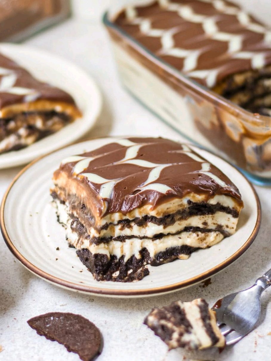 Episode O 'AtoZ of Desserts', a series where every letter unfolds a new delight 💫 If you love Oreo as much as I do, then you are going to love this Oreo Biscuit Pudding 🙌🏻  this eggless pudding recipe will have your heart, I promise ❤️ Ingredients 🥰3 cups + ½ cup milk 🥰5 tbsp cornflour 🥰1 cup fresh cream 🥰1 pouch or ½ cup condensed milk (200ml) 🥰1 tsp vanilla extract For biscuit layer 🥰1 cup milk 🥰25-30 oreos For ganache layer 🥰½ cup dark chocolate 🥰½ cup fresh cream 🥰½ cup white chocolate 🥰3 tbsp fresh cream Instructions 1. Make the cornflour slurry by combining ½ cup of milk with cornflour. Whisk well to remove any lumps. 2. ⁠In a saucepan, add 3 cups milk, cream, condensed milk and vanilla extract heat on medium heat. 3. Once the milk mixture is hot, add the cornflour slurry to this mixture and heat till it starts to thicken. Keep it aside to come to room temperature. 4. To assemble the pudding, take a shallow bowl with 1 cup milk in it. Dip the separated chocolate cookies/biscuits in the milk for a few seconds and then lay them on a serving dish of your choice. Use ⅓ of the cookies for the first layer. 5. Now, take some of the pudding mixture and spread evenly on top of the biscuit layer. 6. Repeat the same process two more times till the serving dish is almost filled. 7. For the ganache, melt the chopped dark chocolate and add room temperature cream to it. Mix well till well combined and smooth. Follow the same process for white chocolate as well. 8. Spread a thin layer of dark chocolate ganache over the pudding, then pipe white chocolate ganache on top. Use a skewer to create the pattern shown in the video. Refrigerate the pudding for 4-5 hours until fully set and serve chilled. #oreopudding #oreo #pudding #creatorsearchinsights 