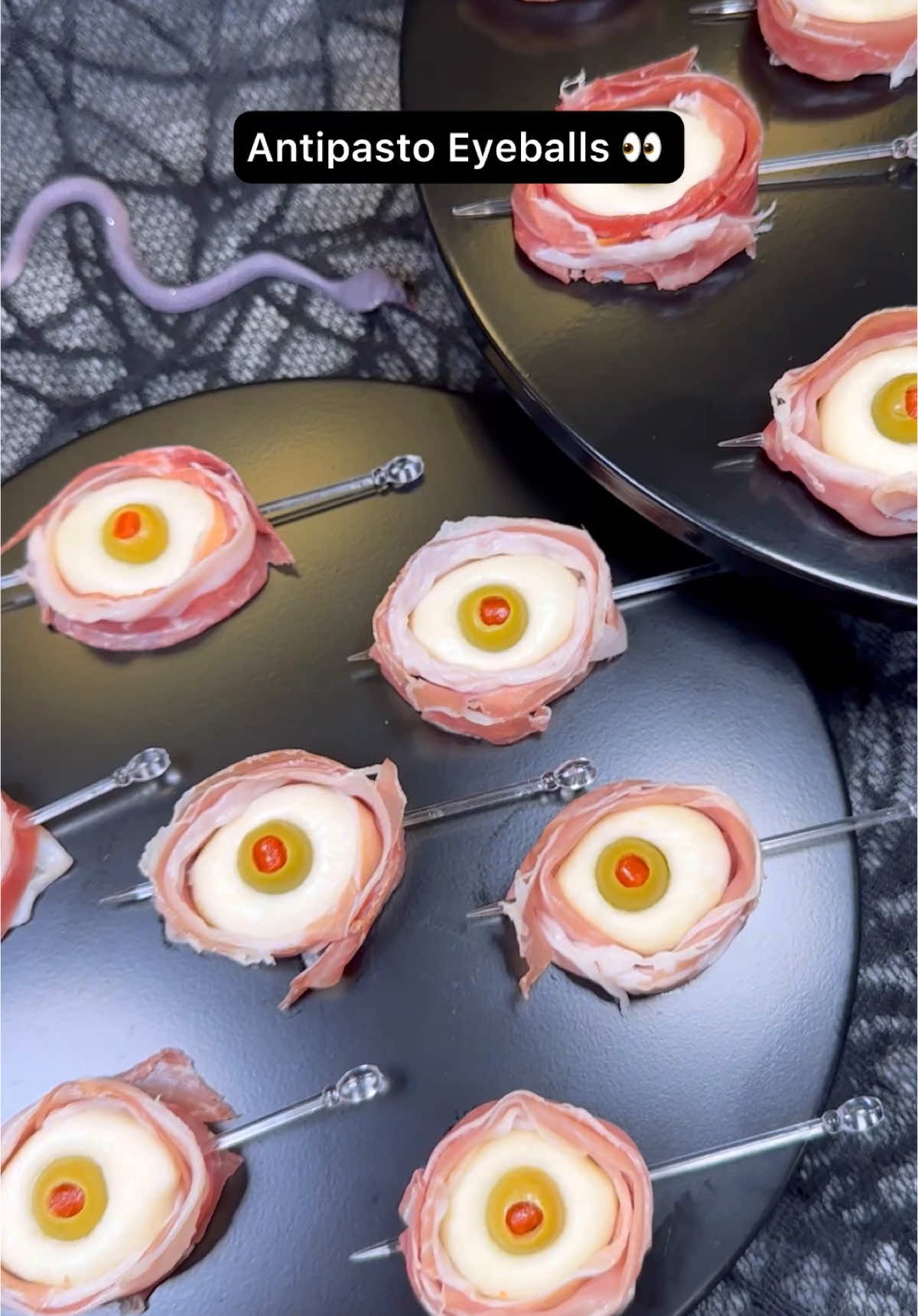 Antipasto Eyeballs 👀🫒🧀 50 Halloween inspired recipes. Who’s making these? Ingredients: 8oz Ciliegine (cherry sized) mozzarella balls  12 Pimento stuffed Manzanilla olives  12 slices prosciutto  Directions: Add mozzarella balls to a bowl and cover with hot water (about 185°F) Allow to sit for 3 minutes to warm the mozzarella enough to shape.  Use two balls to form into 1 larger ball. While still warm, shape into a smooth round ball. Poke a hole in the center using your pinky finger then push in an olive.  Cut prosciutto into 4 long strips and wrap around the mozzarella eyeball. Secure with a skewer Enjoy! 👻 #antipastoeyeballs #halloweenfood #halloweeninspo #edibleeyeballs #halloweenfoodinspo