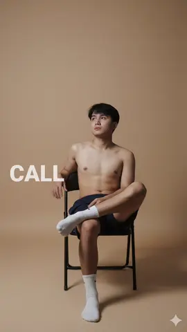 GEMINI AI PROMPT ➡️ Use the model(person in the image) to create a studio photo with the same backgorund color, featuring a young man sitting casually on a metal folding chair with his legs crossed. He is wearing nothing in the top, shorts, and white socks. The lighting is soft and minimal, producing sharp shadows and a moody atmosphere. His pose is relaxed, slightly leaning with one hand on the chair's backrest, his face turned to above. The background is plain, with a simple and modern aesthetic. #CapCut 