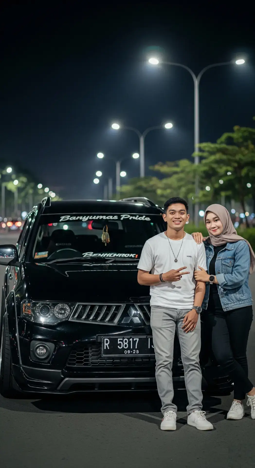 Tutorial  1.Buka Gemini Ai  2.Tambahkan foto ( Tanda + ) 3.Masukan prompt di bawah 👇 ( Bisa modifikasi sesuai keinginan kalian ) 4.Jika hasil mukanya beda, bisa lanjut edit di aplikasi Remakeface ai  Prompt: Edit dua foto ini tanpa mengubah wajah menjadii Sebuah foto malam hari menampilkan sepasang anak muda berpose di depan sebuah mobil SUV hitam merek Mitsubishi Pajero sport. Mobil terlihat menonjol dengan stiker besar di kaca depan bertuliskan “Banyumas Pride”, serta gantungan hiasan tergantung di tengah kaca depan. Plat nomor mobil bernomor R 5817 IJ dengan kode masa berlaku 09•29. Pria di sebelah kiri memakai kaos putih polos, celana panjang abu-abu muda, dan sepatu sneakers putih. Ia tersenyum sambil membentuk tanda perdamaian (peace sign) dengan tangan kanannya. Di lehernya tergantung kalung sederhana. Wanita di sebelah kanan mengenakan hijab berwarna abu-abu muda, jaket denim biru muda di atas kaos hitam, celana panjang hitam, dan sneakers putih. Ia tersenyum sambil merangkul bahu pria di sampingnya dengan tangan kiri. Latar belakang berupa jalan raya malam dengan banyak tiang lampu jalan berjajar, cahayanya terang dan membentuk efek bokeh. Di sisi kanan kiri jalan, tampak pepohonan hijau dan lampu kendaraan yang samar. Suasana foto tampak hangat, ceria, dan penuh kebersamaan dengan nuansa otomotif. #gemini #geminiai #fypシ゚ #ai #trending 