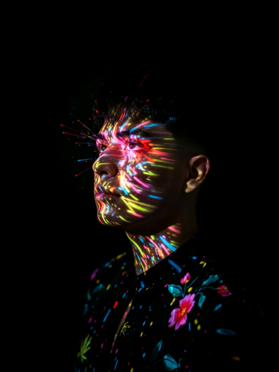 Crea tu propia fotografía con calidad estudio usando Gemini AI.  Prompt en los comentarios. Using this image as a reference: generate a hyperrealistic editorial portrait of the same person, preserving facial structure, skin tone, hair texture, and emotional expression with maximum fidelity. The subject is standing against a deep black background, illuminated by vibrant, multicolored light projections that cover the face and upper torso. The light patterns include dynamic streaks, bursts, and dots in neon tones—pink, cyan, lime green, yellow, red, and electric blue—creating a surreal, energetic atmosphere. The most intense concentration of light is around the eyes, resembling an explosion of color and emotion. The subject wears a minimalist black sleeve with collar with abstract or flower patterns, subtly visible beneath the projected lights. On the body: the light reflections are larger and softer, forming diffuse patches and gradients across the neck, shoulders, and chest Their head is tilted slightly upward, conveying introspection, strength, and poetic tension. The lighting should simulate a real-world projection mapped onto the skin, with realistic shadows, reflections, and color blending. Maintain sharp focus on the eyes and facial features, with cinematic depth of field and soft bokeh in the background. Style: editorial portrait with surreal and ritualistic undertones.   Camera: full-frame DSLR simulation, 85mm lens, f/1.4 aperture, ISO 100, shutter speed 1/125s.   Lighting: simulated projection mapping with high-contrast multicolor beams.   Color grading: rich, saturated tones with deep blacks and glowing highlights.   Resolution: ultra-high (8K equivalent), suitable for print and exhibition.   Mood: emotionally charged, visually captivating, empowering, and inclusive. --v 5 --ar 3:4 --style raw --quality 2 --ref_photo #geminiai #prompt #inteligenciaartificial #photostudio 