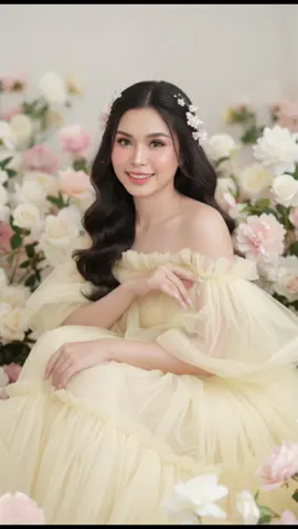 💛A dreamy, romantic portrait of a young woman surrounded by soft pastel flowers, sitting gracefully in a delicate pose. She wears a flowing off-shoulder gown made of sheer pale yellow tulle, with layers of soft fabric creating a light and ethereal look. #แจกคําn#แจกคําสัir cascades down naturally, decorated with small delicate flowers tucked into the strands. Makeup is flawless and doll-like: glowing porcelain skin, soft blush on the cheeks and nose, glossy pink lips, and large luminous eyes with long eyelashes, giving her an enchanting and fairy-like beauty. Her long manicured nails are elegantly styled, enhancing the sophisticated vibe. The soft studio lighting creates a gentle, glowing atmosphere with no harsh shadows, making the skin appear smooth and radiant. The background is filled with blurred pastel flowers (white, pink, and cream tones), enhancing the dreamy, romantic, and fantasy-like mood. By using the extract same face from the reference image