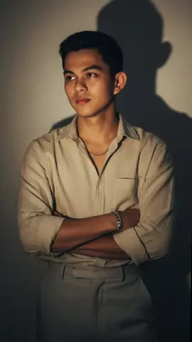 Gemini AI PROMPT: 1. Open Gemini App/Website 2. Upload Your Photo 3. Copy & Paste this prompt: Create a highly realistic portrait of young man standing in front of a softly lit wall, with his arms crossed naturally. He is wearing a light beige, slightly oversized button-up shirt tucked into high-waisted, light grey trousers. The shirt is slightly wrinkled and open at the collar, revealing a thin silver necklace. He also wears a chunky silver bracelet on his right wrist. His expression is calm and contemplative, gazing slightly to the left with gentle shadows falling across his face. Behind him, two distinct shadows are cast on the wall: one is dark and the other is a warm tone (light yellow/orange), due to mixed directional lighting. The lighting is soft but dramatic, giving the image a moody, cinematic feel. The background is minimal, emphasizing the subject and the artistic shadow play. #gemini #prompt #aesthetic #photography #ai