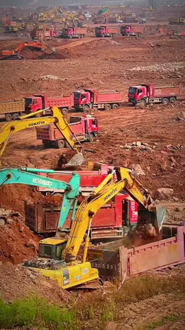 A massive construction site buzzes with activity, as Komatsu and Kobelco excavators load earth into red dump trucks, showcasing large-scale earthmoving operations. #MassConstruction #KomatsuExcavator #KobelcoExcavator #DumpTruck #Earthmoving
