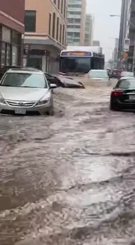 Flash Flood Sweeps Through Downtown Streets Minneapolis, Minnesota — April 3, 2025 A sudden and intense spring rainstorm overwhelmed city drainage systems Tuesday afternoon, turning busy metropolitan thoroughfares into treacherous rivers. The rapidly rising waters caught many commuters by surprise, leaving several vehicles stalled and partially submerged as the current took hold of the urban landscape. Dramatic footage captured at a major intersection shows a city transit bus attempting to navigate the high waters, inadvertently creating a massive wake. This surge of water pushed several stalled sedans into one another, causing them to drift helplessly and collide. Spectators on the sidewalk can be heard shouting in shock as a silver car is lifted by the force of the water and wedged against a nearby white SUV, illustrating the sheer power of the flash flood. Local emergency services responded to numerous calls for water rescues and stalled vehicles throughout the afternoon. While no major injuries have been reported, city officials are warning residents to avoid driving through standing water, noting that even a small amount of moving water can be enough to displace a vehicle and create life-threatening conditions. Cleanup efforts are currently underway as water levels begin to recede. This video is created using AI, and the story is for your entertainment.