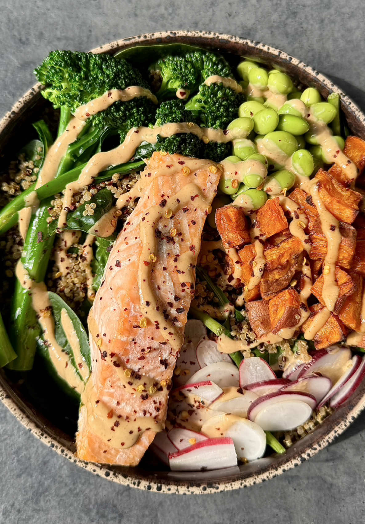 Welcome to High Protein Meals Episode 1: The Rainbow salmon bowl. A healthy, high protein, nutritious meal full of goodness 😍 Protein 45g | Kcal 705g per serving In this brand new series we’ll be showing you how to make delicious and quick, high protein meals. They are easy to cook and will leave you feeling satisfied and nourished after a long day. Think indulgent pastas, decadent rice bowls, baked crispy chicken, pimped up ramen and so much more. If this sounds like your kinda thing, give us a follow to stick around for the tasty recipes coming your way.   Serves 2 Ingredients:  - 2 tbsp smooth peanut butter - 1-2 tbsp water - 1 lime juiced - 1 tsp honey - 1 tbsp soy sauce - 1/2 tbsp ginger - 2 salmon fillets - 1 large sweet potato - 90g edamame - 100g radishes - 100g broccoli - 200g quinoa - 100g spinach - 1 tbsp chilli flakes - 1tbsp olive oil - salt & pepper Method:  1. Preheat oven to 180c  2. Chop up your sweet potatoes into 2cm chunks, cover with 1/2 tbsp olive oil and salt and put into the oven for 30 minutes 3. Put the salmon on a baking tray and sprinkle with salt and 1/2 tbsp olive oil, then put in the oven at for 15 minutes  4. Blanch the broccoli in boiling water for 1-2 minutes and then add into cold water  5. Thinly slice the radishes 6. Mix the peanut butter, lime juice, soy sauce, honey and ginger paste in a bowl and then add in 1tbsp water until the consistency is light and creamy (can add more water if needed)  7. Plate up the spinach, quinoa, radishes, broccoli, sweet potatoes, edamame 8. Add the salmon and drizzle sauce on top, finish with a pinch of chilli flakes 
