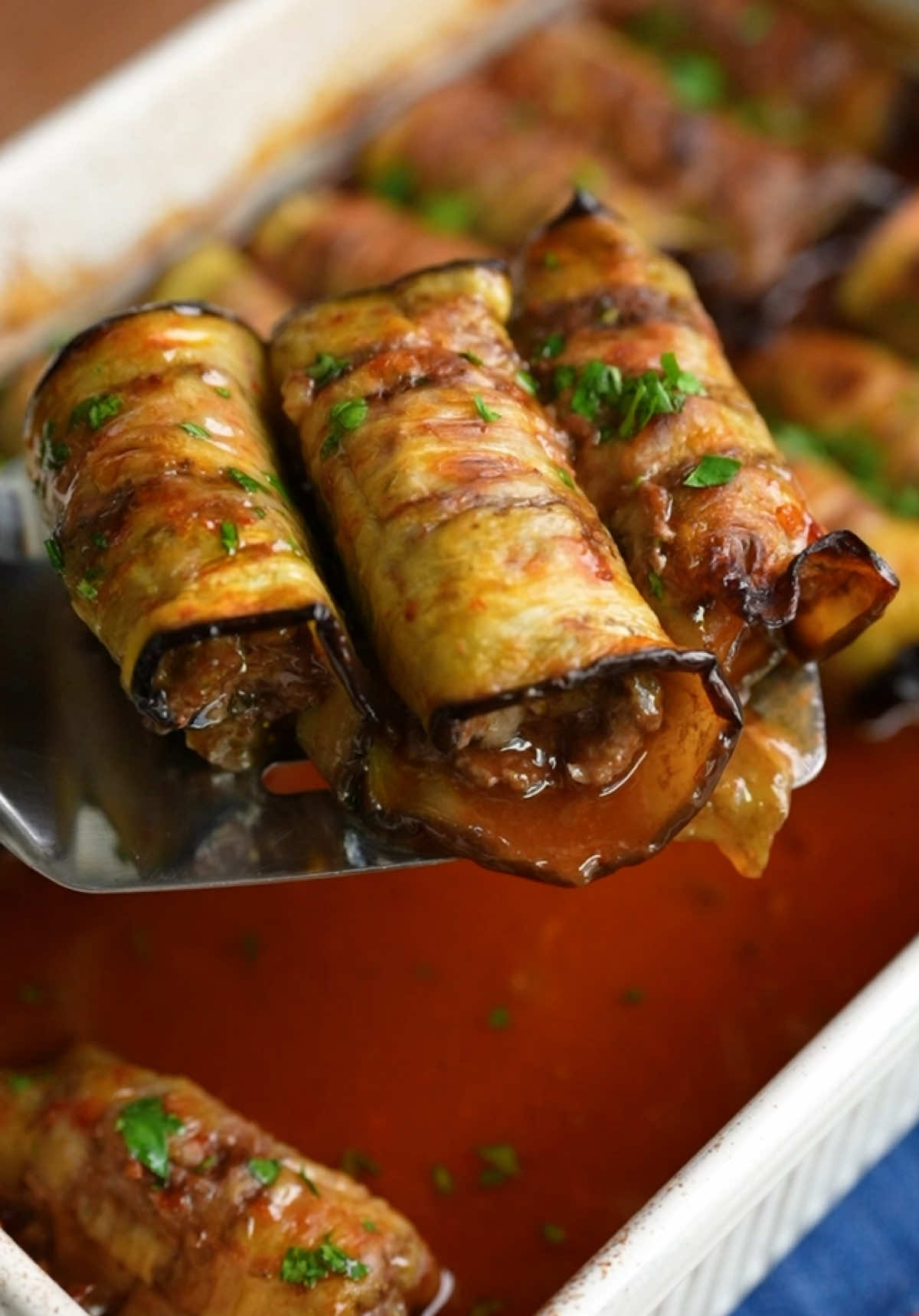 Kıymalı Patlıcan Sarma 🤌🏻😋 Az yağ ile kızartma lezzetinde kıymalı patlıcan sarma hazırladık! 🤤 Denemek için kaydetmeyi unutmayın! 📌 📲 Detaylı tarife, deneyenlerin yorum ve fotoğraflarına Nefis Yemek Tarifleri uygulamasında “Kıymalı Patlıcan Sarma” araması yaparak ulaşabilir, siz de bu nefis tarifi defterlerinize ekleyebilirsiniz. 📙✨ Malzemeler 2 adet bostan patlıcan Sıvı yağ Kıymalı harcı için; 600 g kıyma 1 adet kuru soğan Çeyrek demet maydanoz 1 tatlı kaşığı tuz 1 tatlı kaşığı toz kırmızı biber 1 çay kaşığı pul biber Yarım çay kaşığı kimyon Yarım çay kaşığı karabiber Sosu için; 1 yemek kaşığı domates salçası 1 tatlı kaşığı biber salçası 1 yemek kaşığı nar ekşisi 1 yemek kaşığı sıvı yağ 2 su bardağı sıcak su (400 ml) 1 çay kaşığı tuz Hazırlanışı Bostan patlıcanları ince ince dilimledikten sonra 15-20 dakika tuzlu suda bekleterek acısının çıkmasını sağlayalım. Patlıcanları mutfak havlusu ile iyice kurulayıp fırın tepsisine dizelim. Arkalı önlü çok az yağlayalım ve önceden ısıtılmış 190 °C fırında 15 dakika pişirelim. Kıymalı harcı için karıştırma kabına kıyma, rendeleyip suyu sıkılmış soğan, ince kıyılmış maydanoz, tuz ve baharatları alarak güzelce yoğuralım. Patlıcan dilimlerinin üzerine harçtan alarak yayalım ve rulo şeklinde saralım. Fırın tepsisine aldığımız patlıcan ruloların üzerine tüm malzemeleri karıştırarak hazırladığımız sostan gezdirelim. Islattığımız pişirme kağıdı ile de üzerini kapatarak önceden ısıttığımız 180 °C fırında, alt üst fansız ayarda 30 dakika pişirelim. Sürenin sonunda üzerinden pişirme kağıdını alıp 10 dakika daha pişirerek fırından alalım ve sıcak sıcak servis edelim. Afiyet olsun! #nefisyemektarifleri #tarif #bugünnepişirsem #food #TiktokMutfağı 