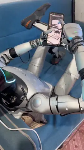 A humanoid robot relaxing on the couch and scrolling through videos like a human. Could robots eventually learn our habits too? #HumanoidRobot #HumanoidRobots #Robotics #Al #ArtificialIntelligence Future Tech Automation Innovation less